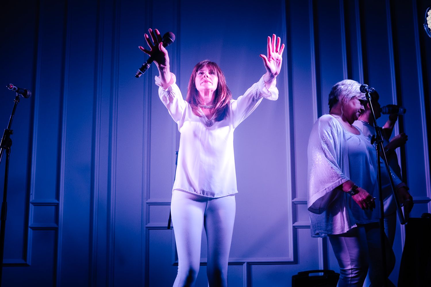 A person in a white dress performs an expressive dance sequence under dramatic blue stage lighting.
