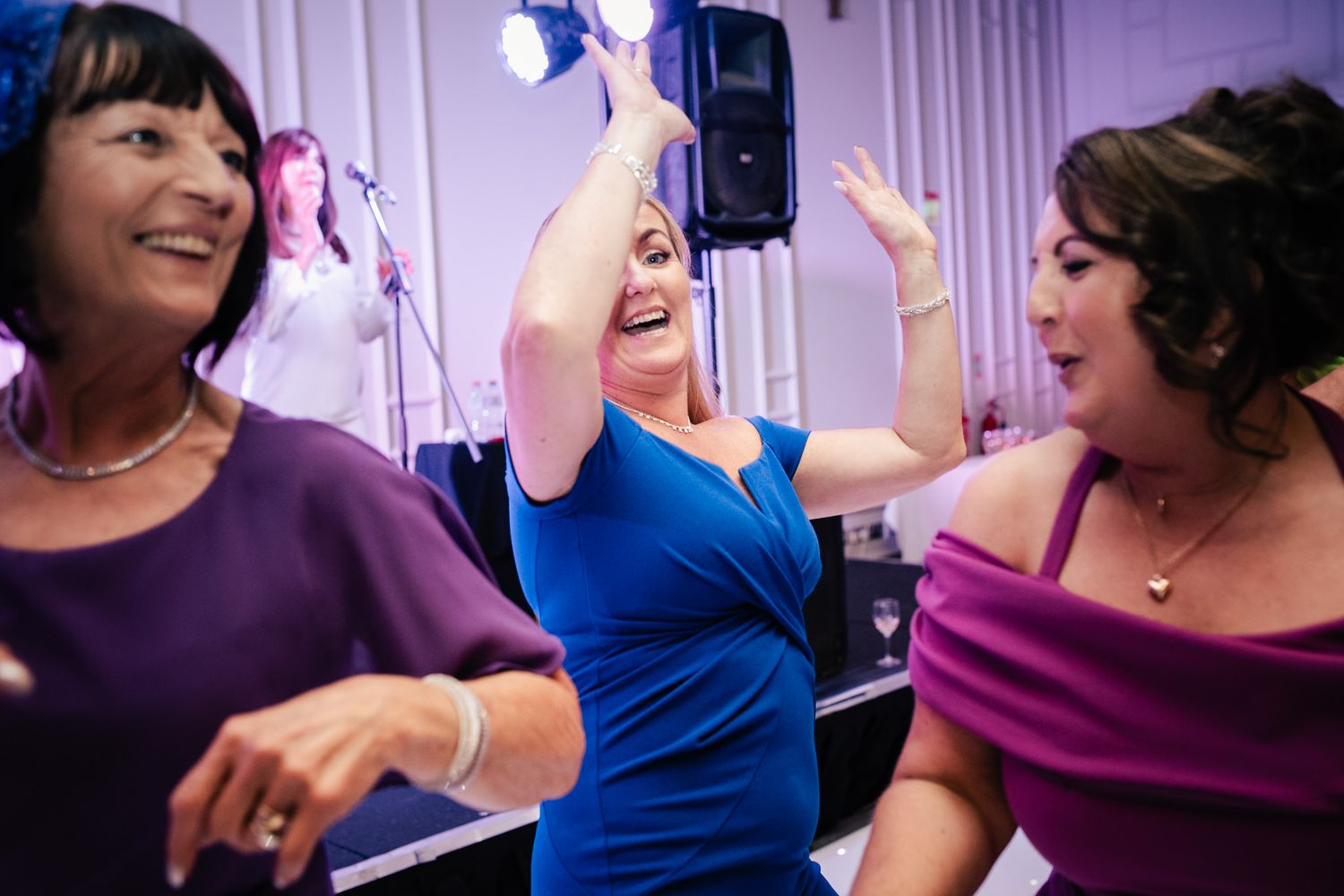 Party guests in colorful dresses dance and celebrate together on the dance floor with joyful expressions.