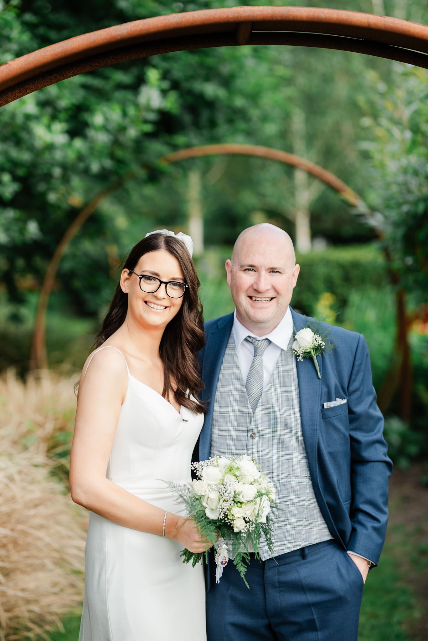 Wedding portrait under decorative garden arch with lush greenery.