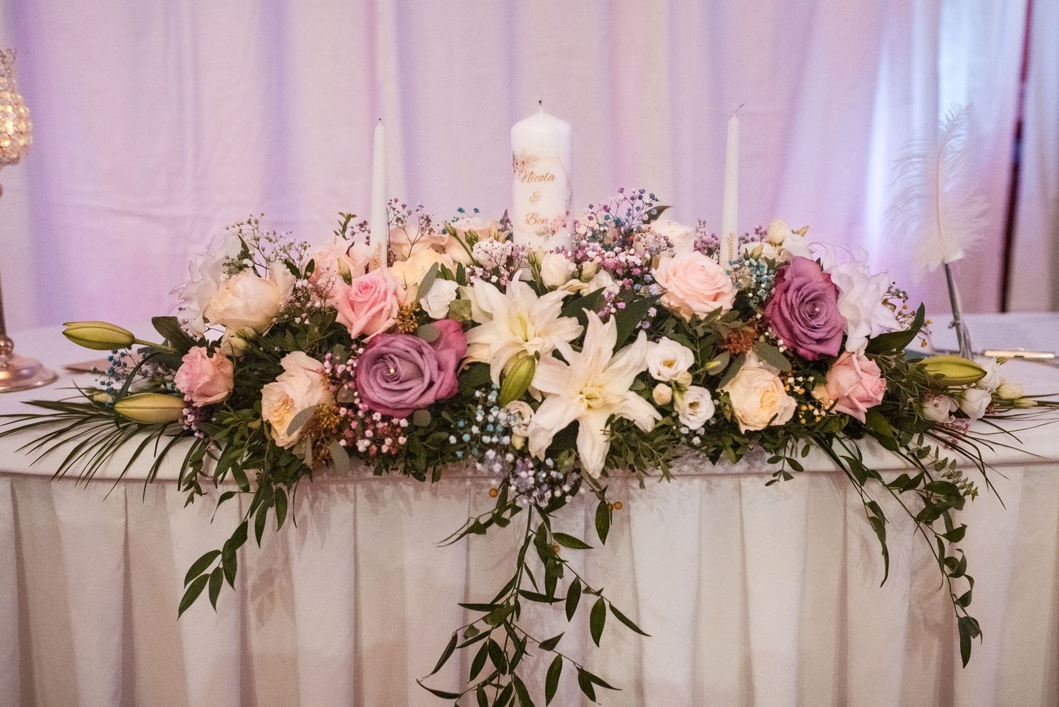 Elegant floral arrangement with lilies, roses, and greenery adorning a wedding head table.