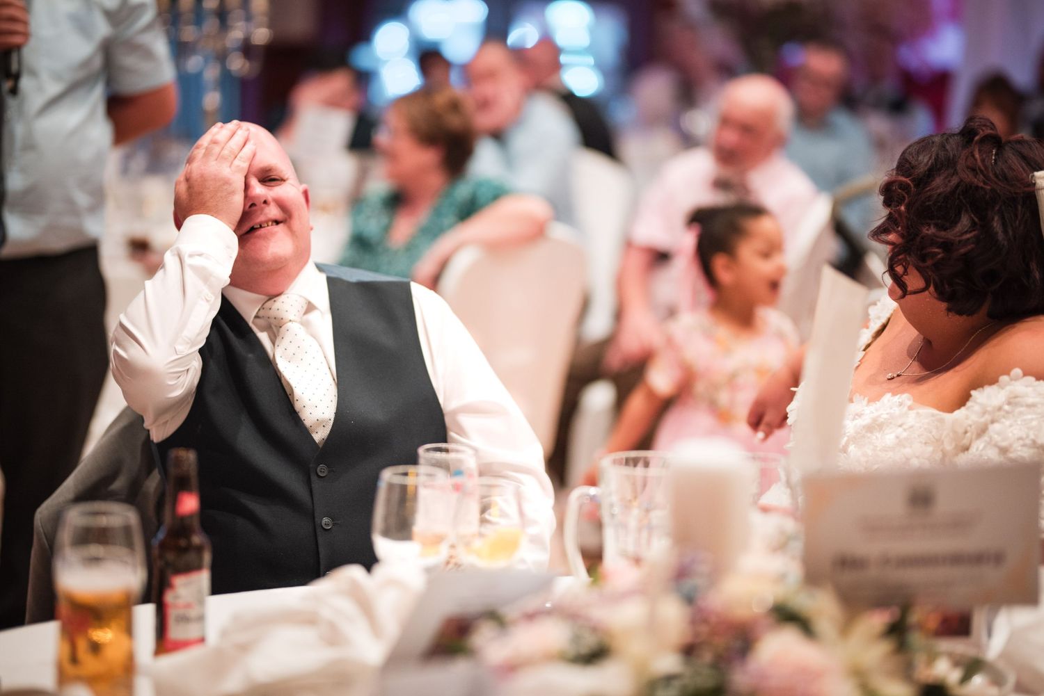 Wedding guests seated at reception tables react with joy and laughter during emotional wedding speeches.