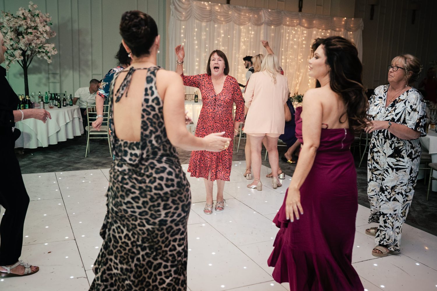 People dancing on a tiled floor at a celebratory event with formal attire and festive atmosphere.