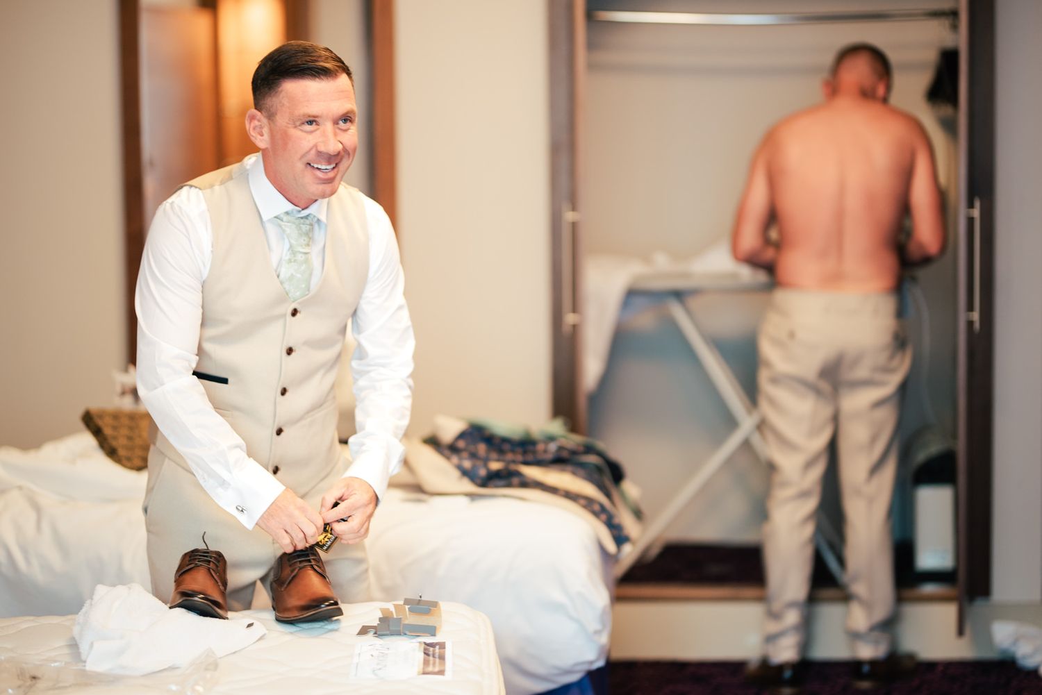 A person in formal attire smiles while getting dressed in a hotel room.