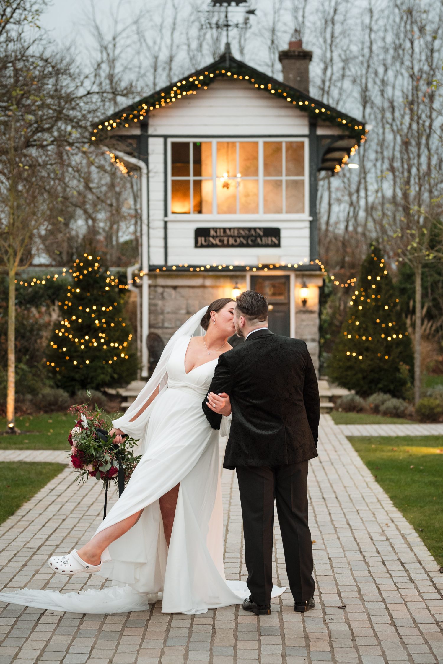 Dancing couple share a romantic moment outdoors at holiday venue with twinkling lights and scenic architecture.