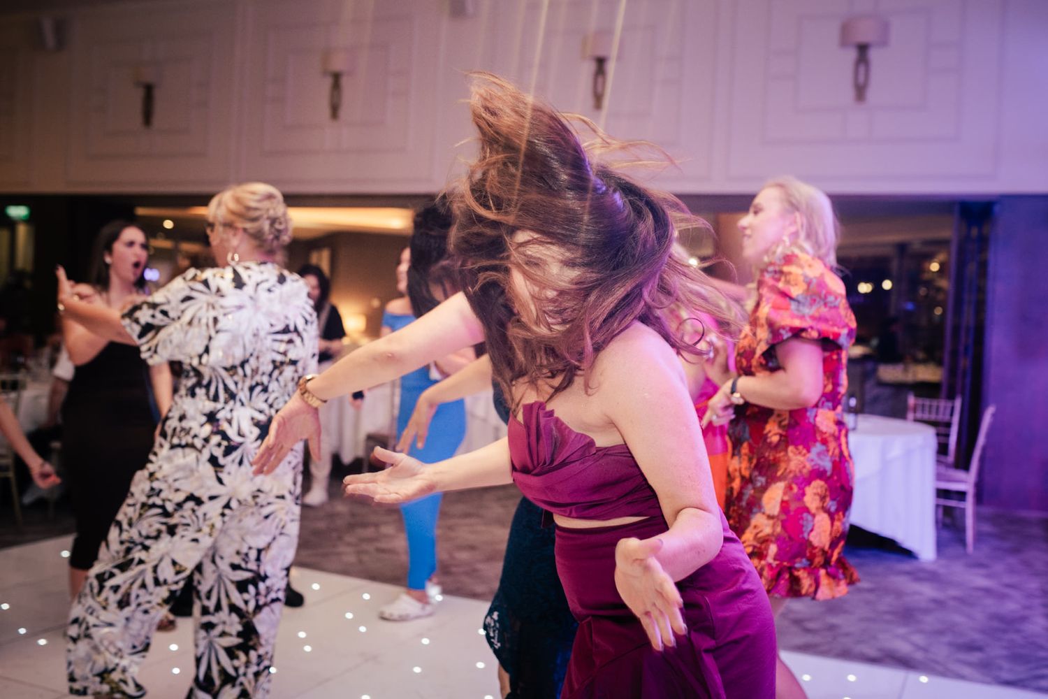 People dancing to lively music during a celebratory event in an indoor venue with purple lighting.