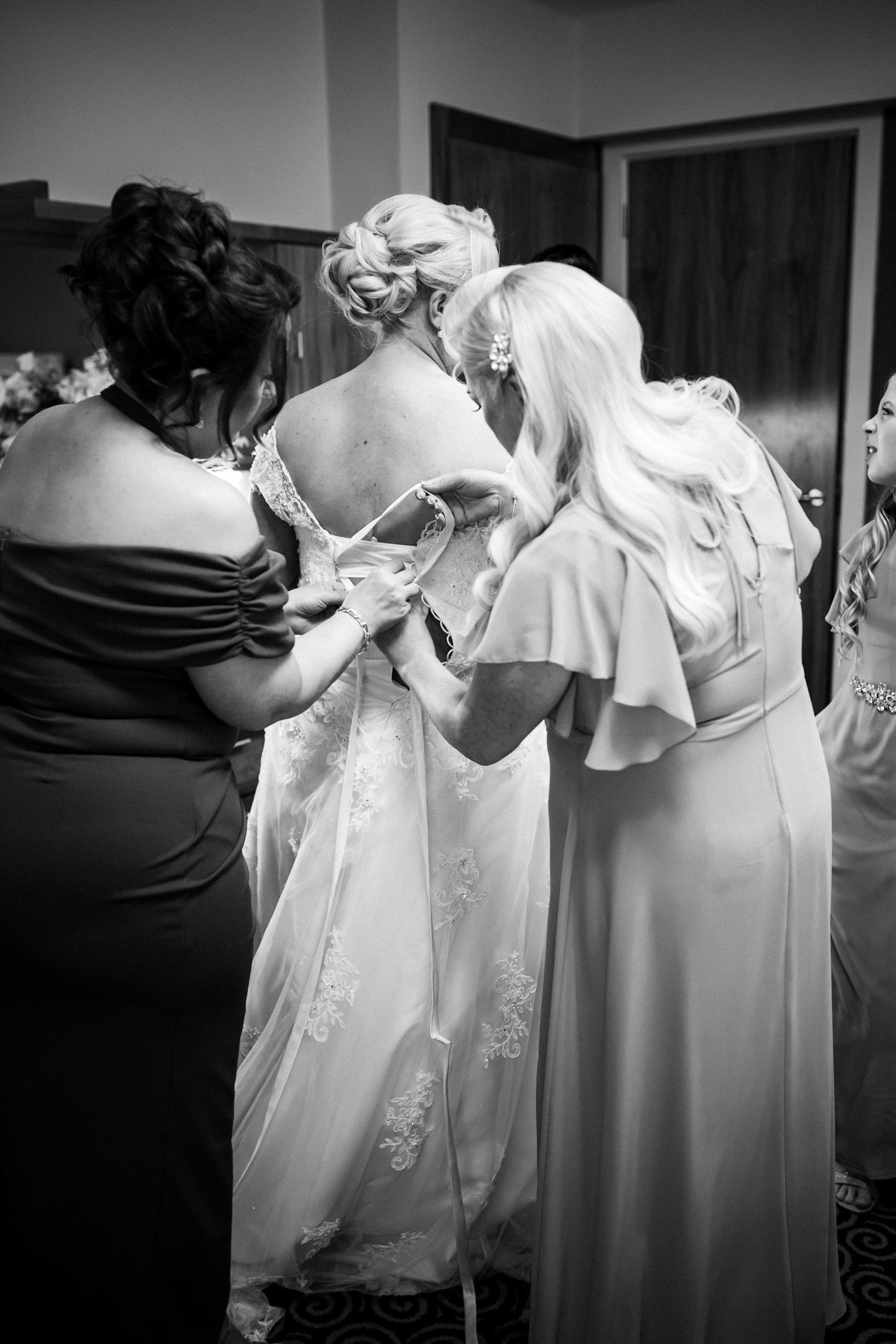 A black and white photo series showing close-up details of a formal white wedding gown being fitted and adjusted.