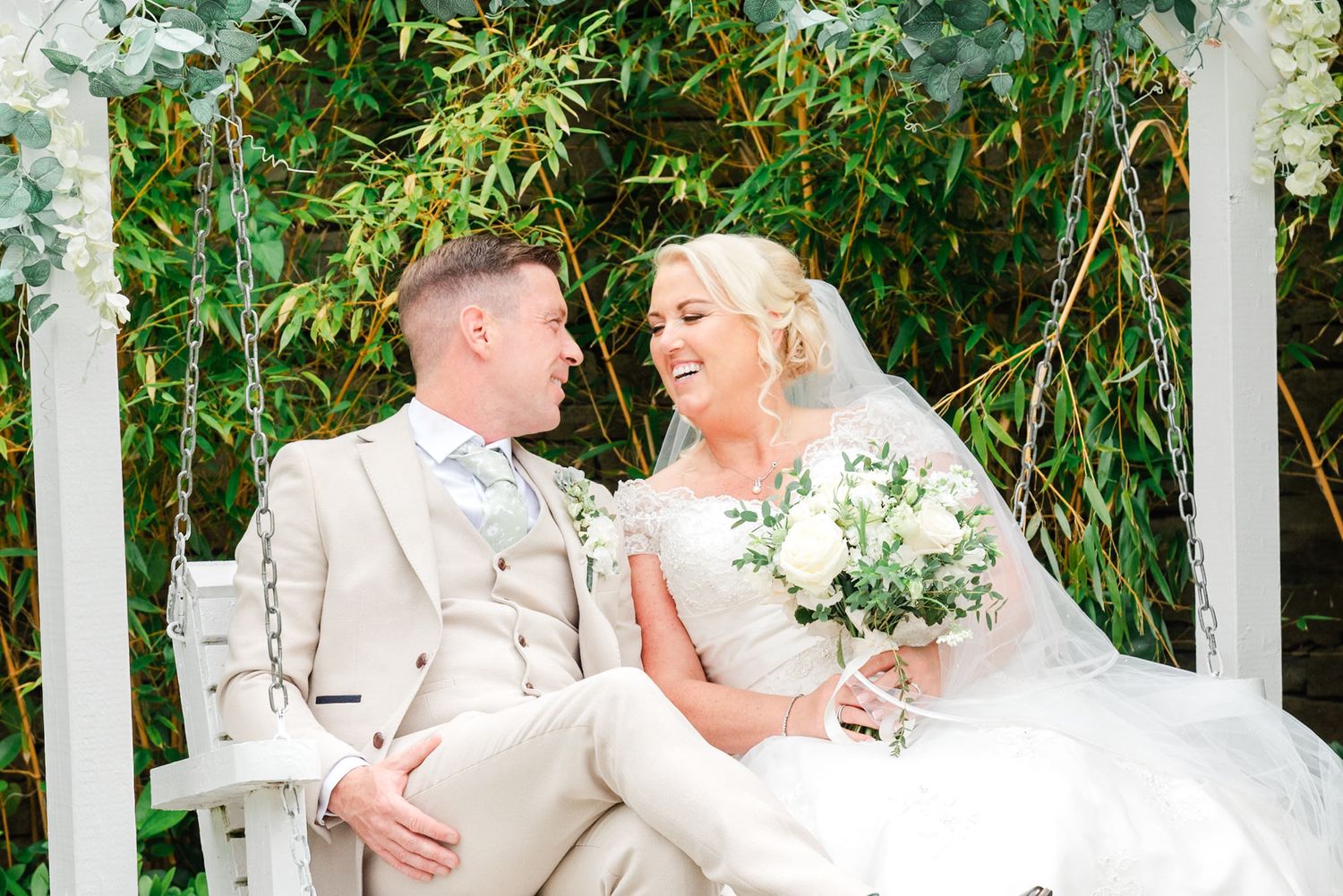 Bride and groom sharing intimate moments during photo session in front of white pillars and bamboo trees.