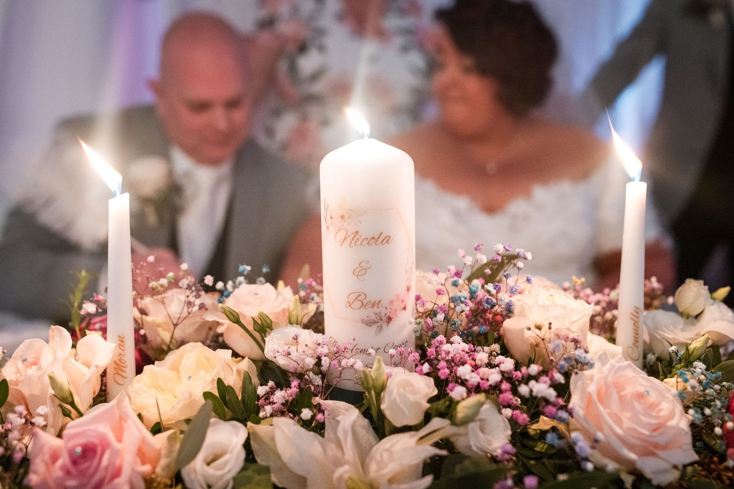 White candles illuminated among pink and white floral arrangements create an elegant wedding reception table centerpiece.