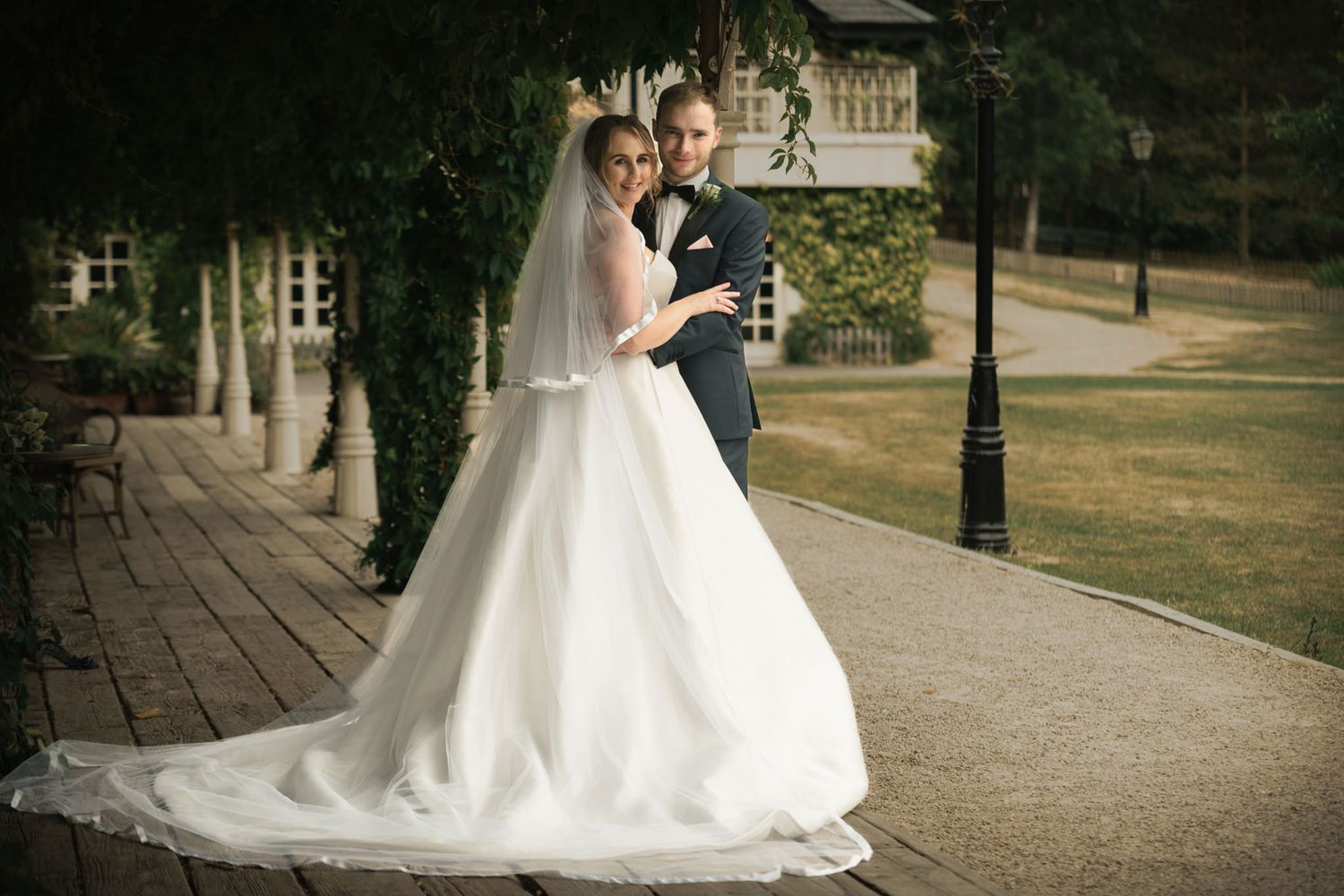 Wedding couple embracing on wooden walkway with garden backdrop.