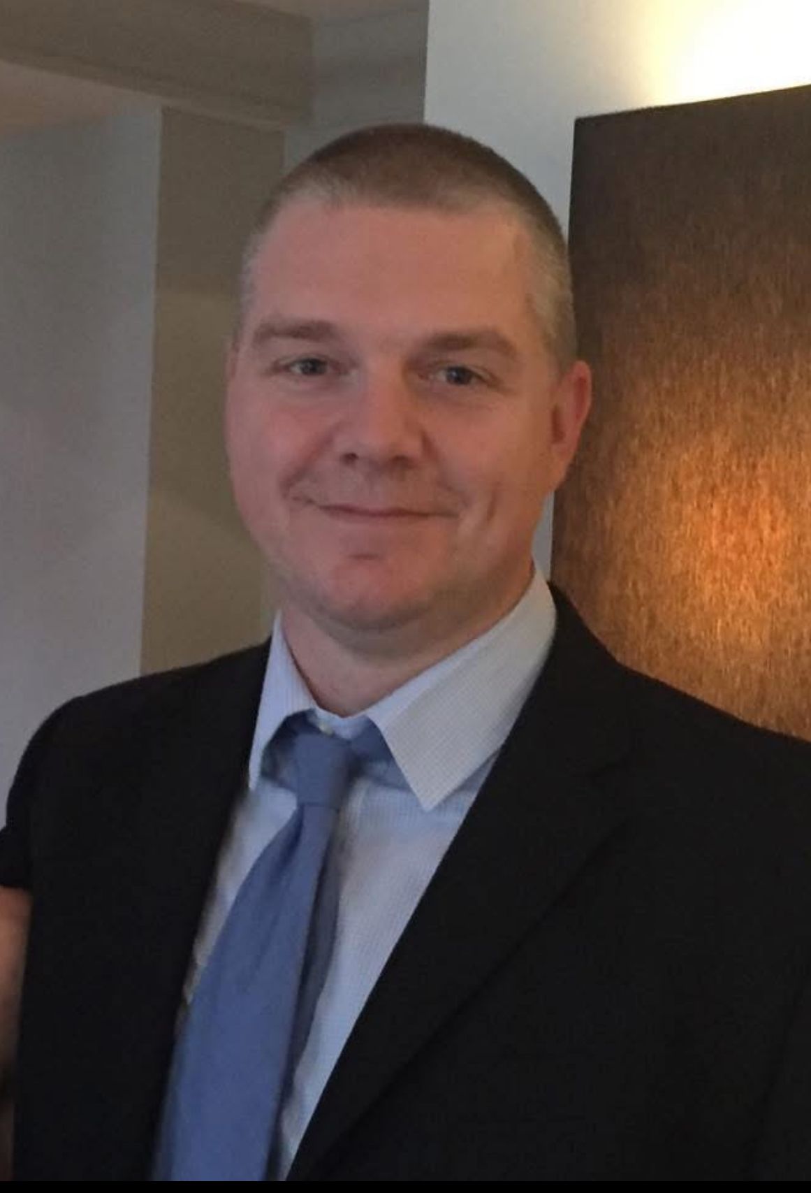A professional business portrait in formal attire against a warmly lit background.