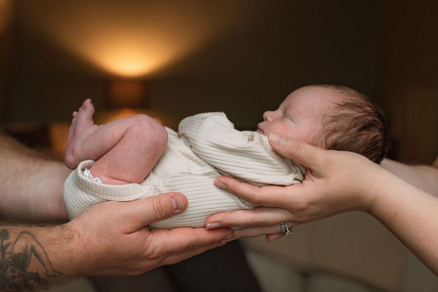 Mother and father's hands hold their newborn baby.