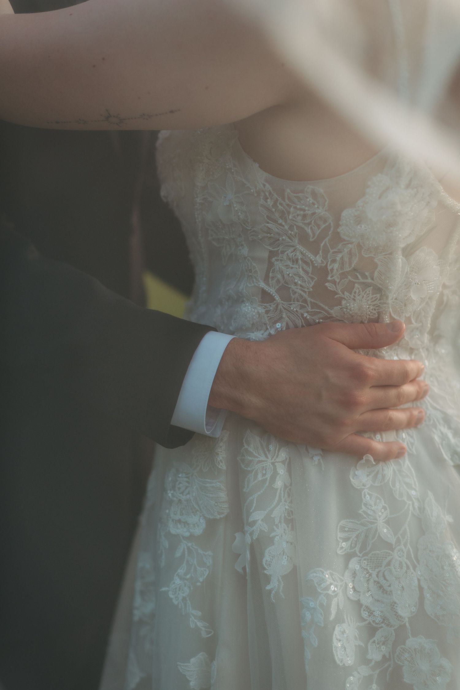 Close-up of hands embracing waist showing intricate lace detail of wedding dress.