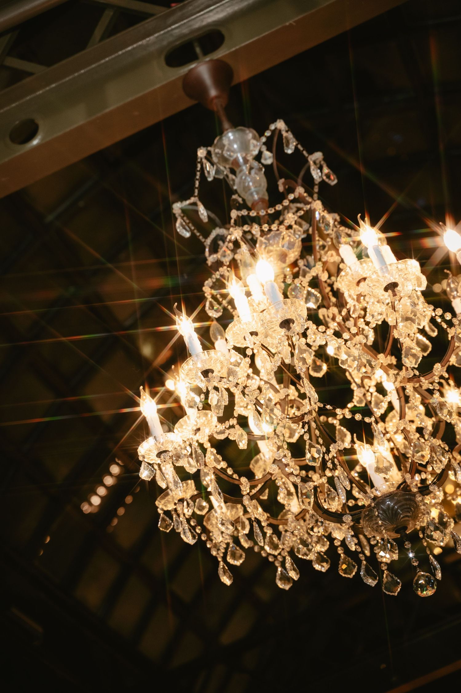 Ornate glass chandelier emanates warm light with cascading crystal drops creating an elegant glow against a dark ceiling.