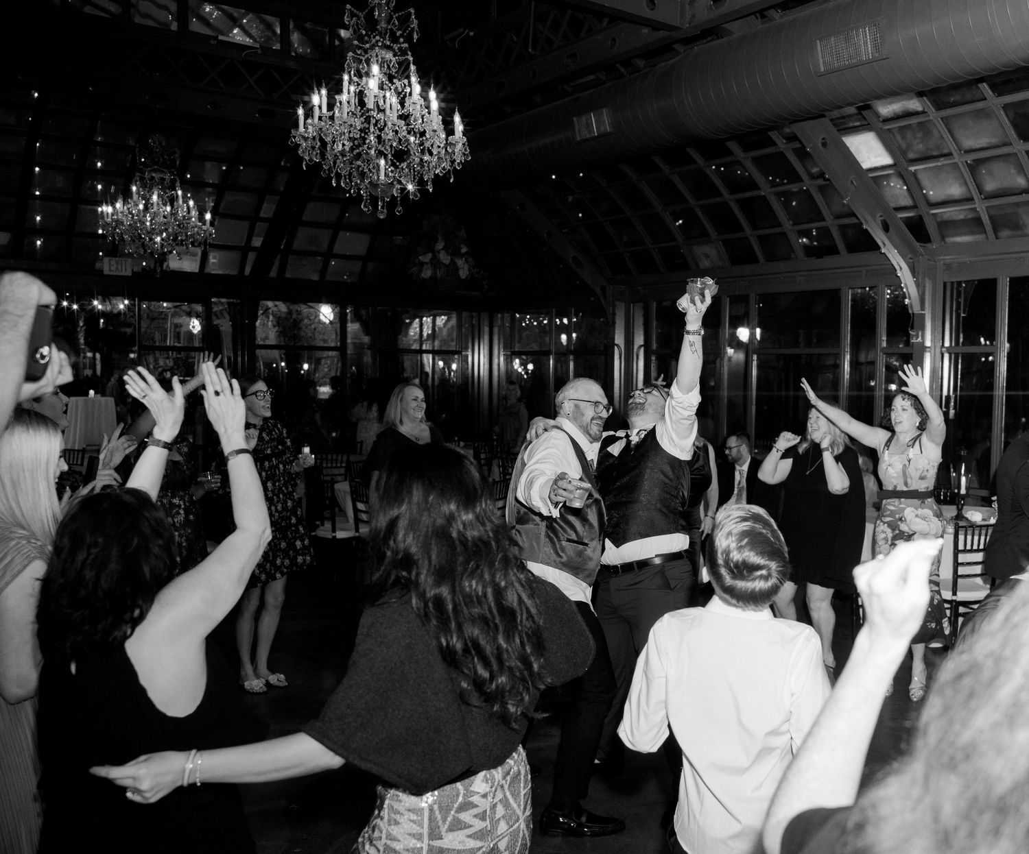 A series of black and white photos showing people dancing and celebrating in a dimly lit venue with chandeliers overhead.