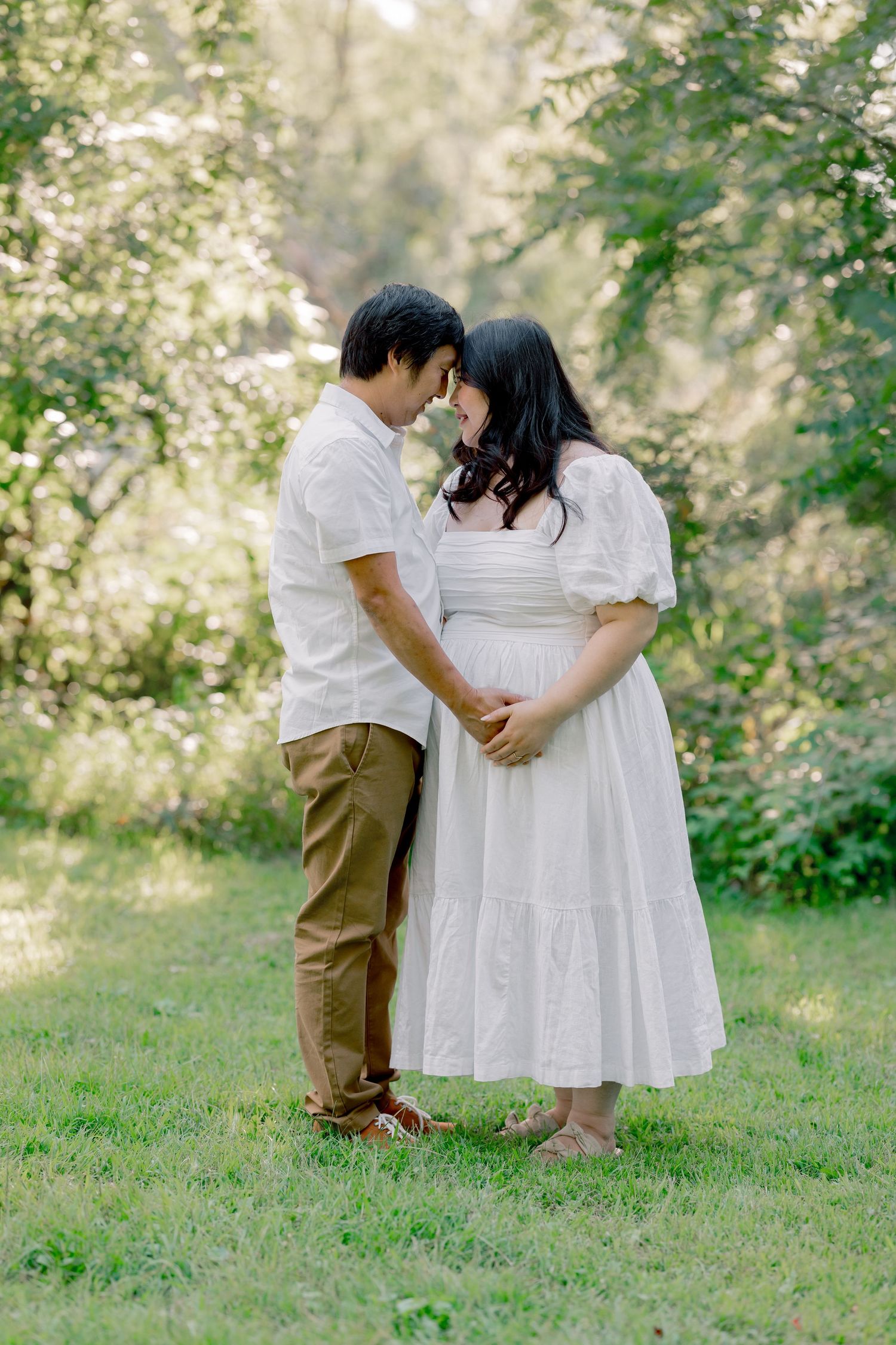 A romantic couple in white outfits shares an intimate moment together in a sunlit garden setting.