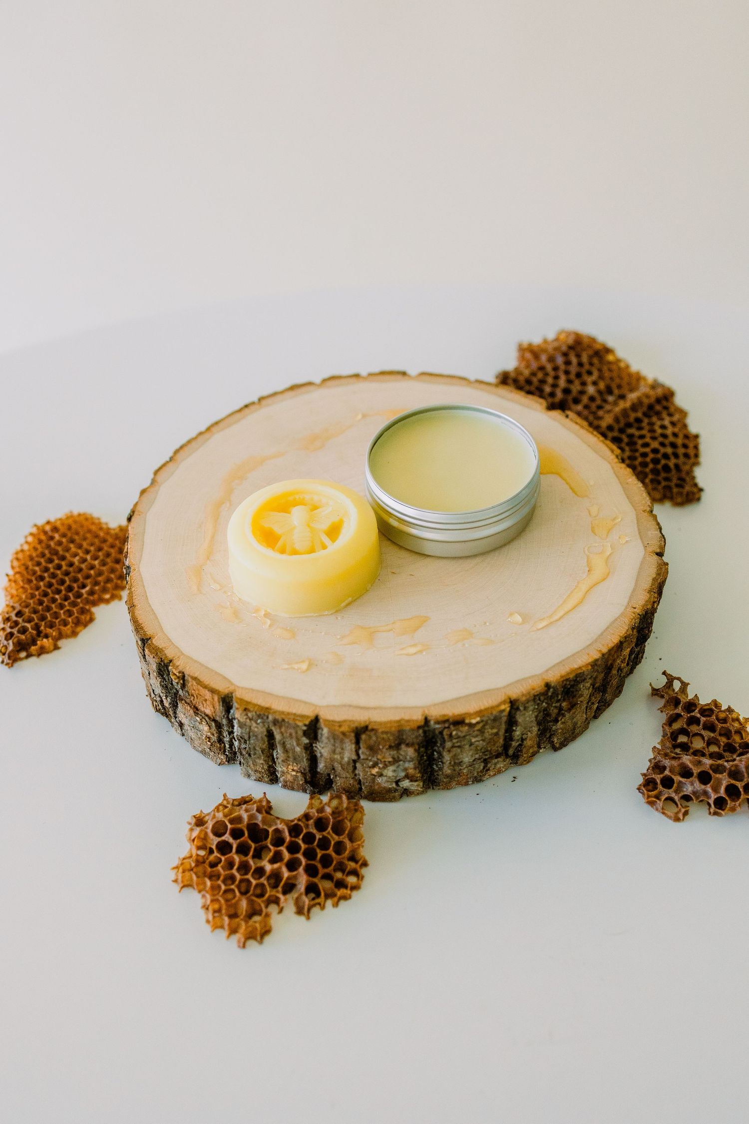 Natural beauty products displayed on a rustic wood slice with honeycomb pieces arranged around balms and salves.