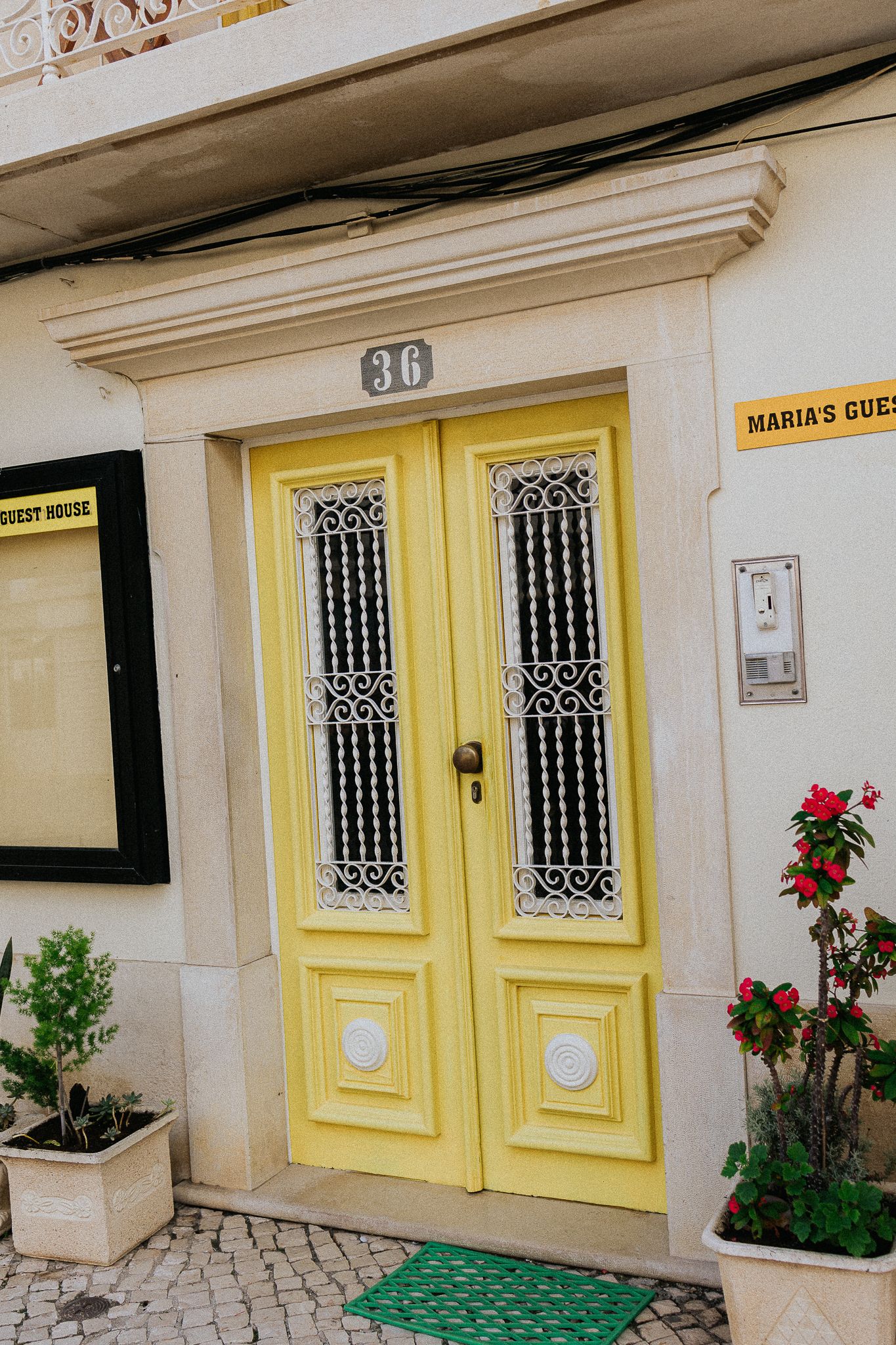 Yellow double door with ornate metalwork and the number 30, flanked by potted plants on a white building.