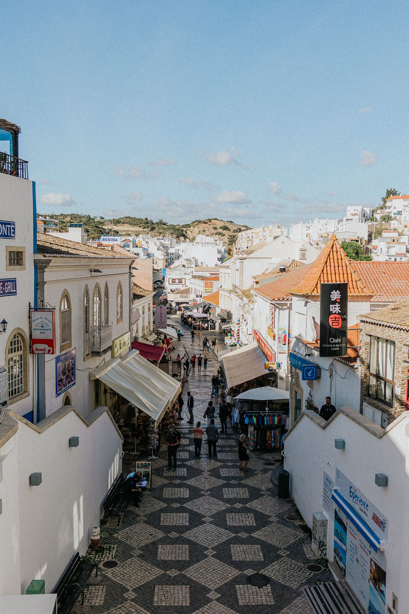 Picturesque cobblestone street lined with white buildings and shops in old town Albufeira, Portugal on sunny day.