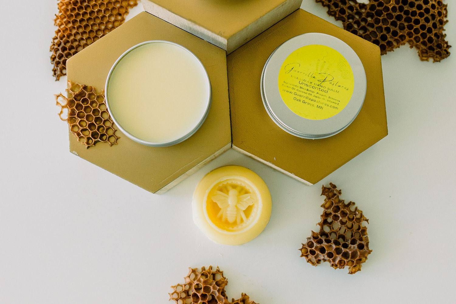 Handmade beeswax candles and coffee beans arranged on golden hexagonal platforms against white background.