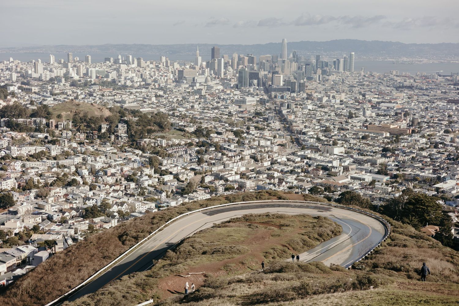 Aerial view of San Francisco cityscape with Twin Peaks and a curved road in the foreground.
