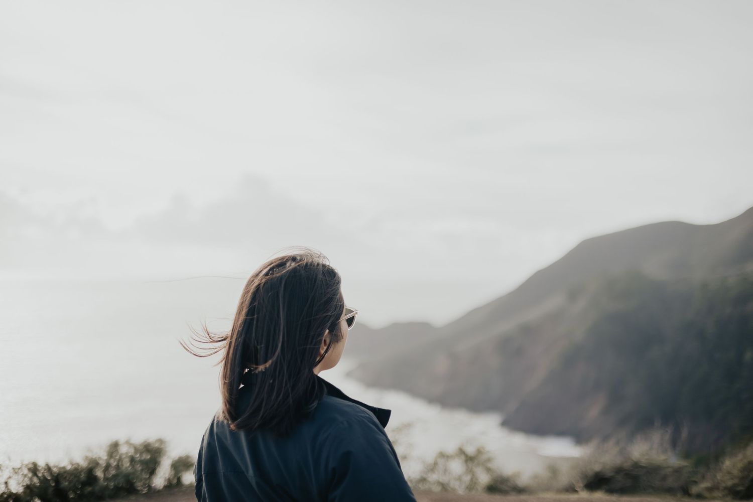 Person looking out at foggy coastal mountains from scenic viewpoint.