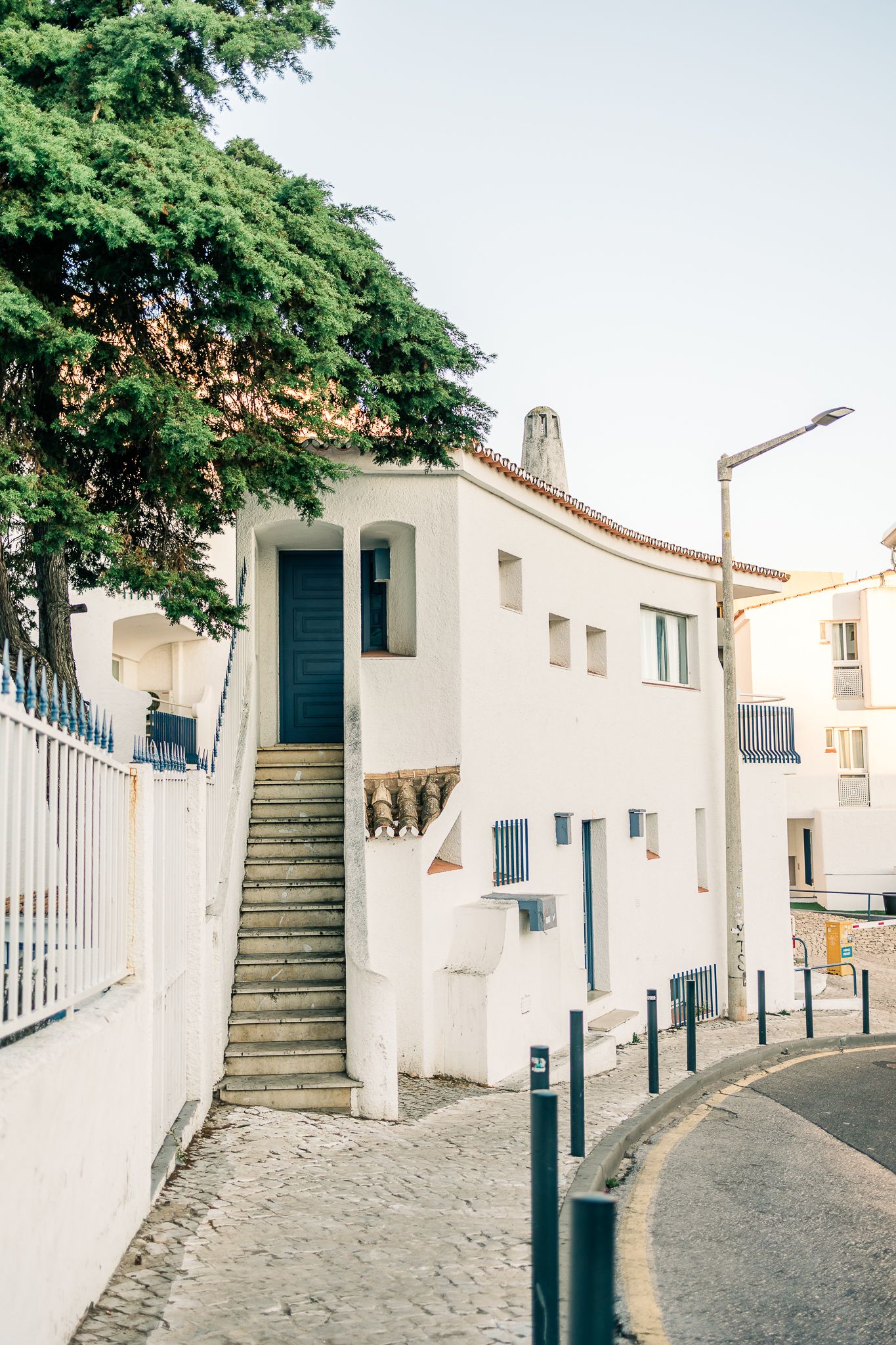Charming whitewashed Mediterranean house with blue shutters and outdoor staircase along a curved cobblestone street.