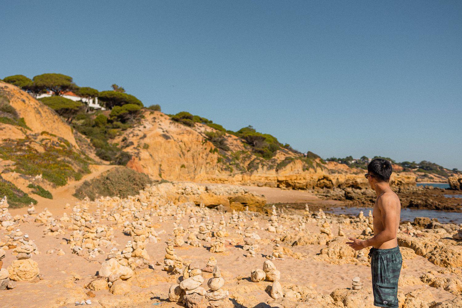 Person looking out at scenic rocky beach coastline with orange cliffs and blue sky in Portugal.