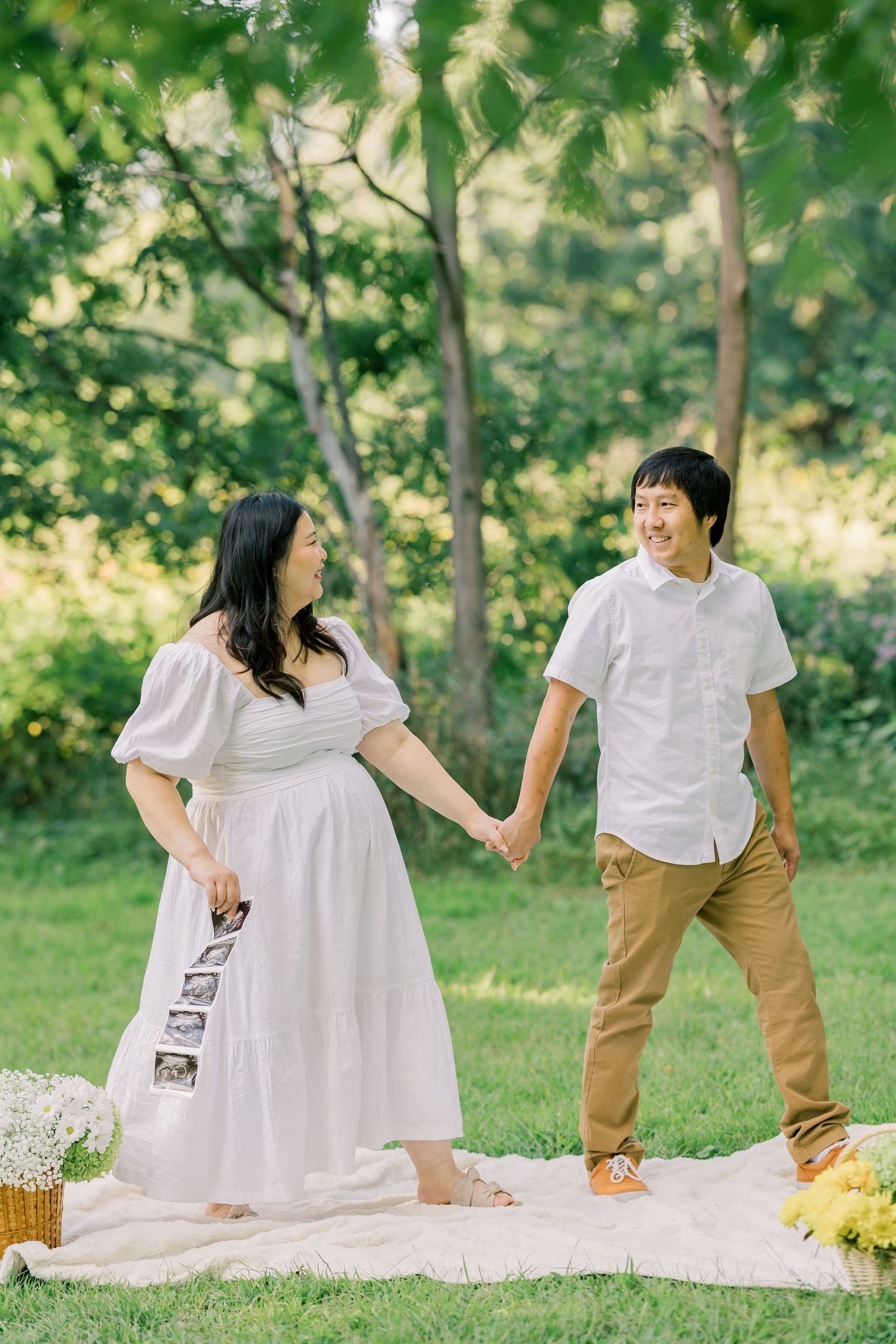 A romantic outdoor picnic scene with a white blanket and wicker basket in a lush green park.