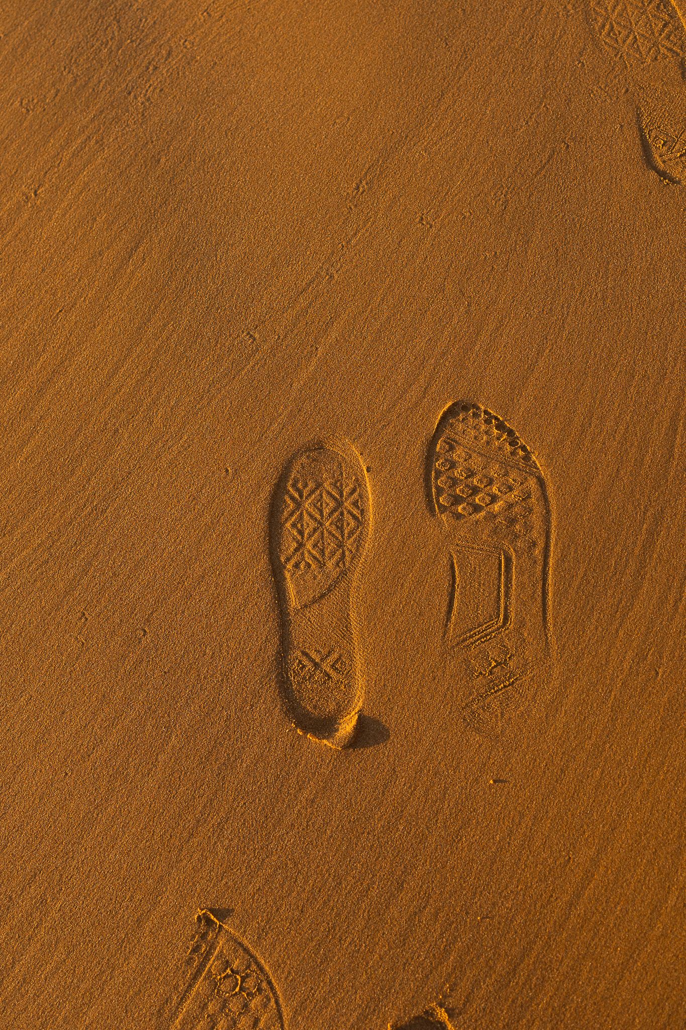 Shoe prints imprinted in smooth orange sand with distinctive tread patterns visible in the desert texture.