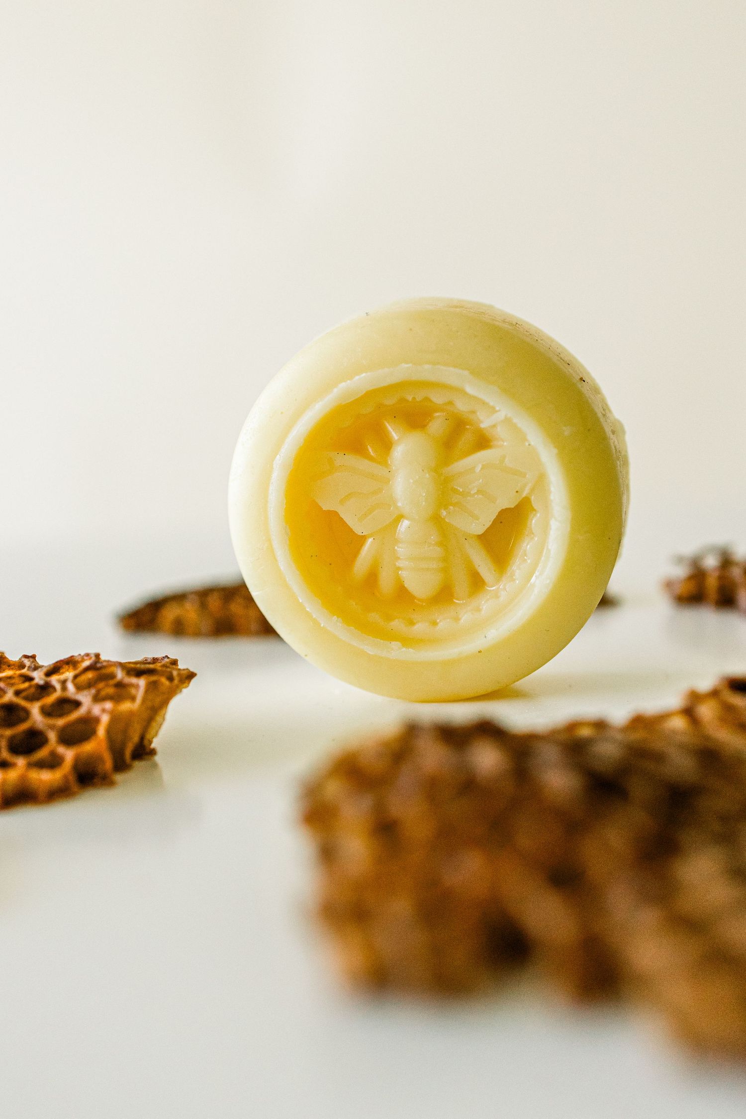 A yellow beeswax soap bar with embossed honey bee design shown with natural honeycomb pieces in the background.