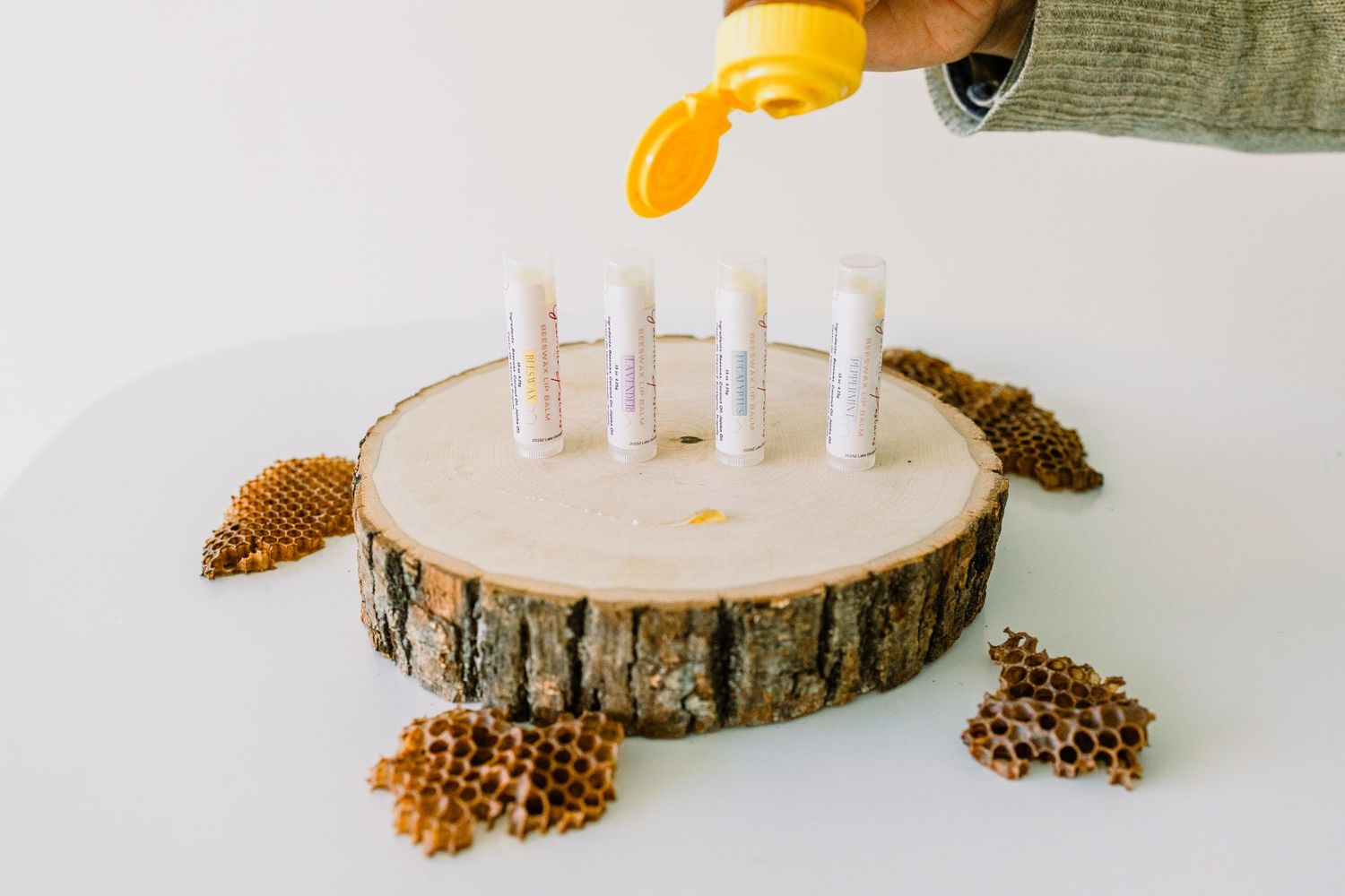 Yellow liquid being poured onto natural wood slice candle holder with three white candles and pinecone decorations.