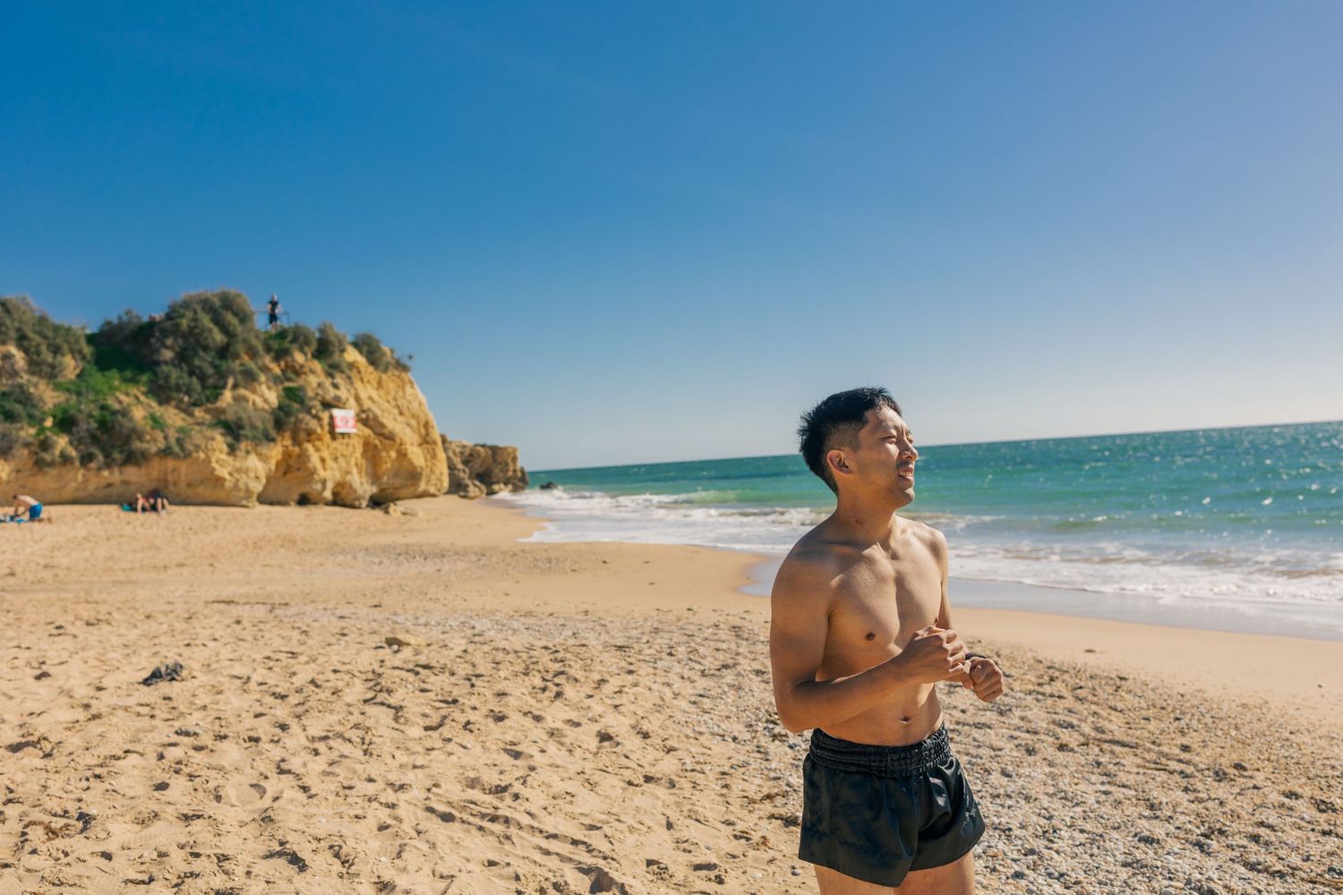 Person standing on a sandy beach with rocky cliffs and blue ocean waters under clear skies in Portugal.