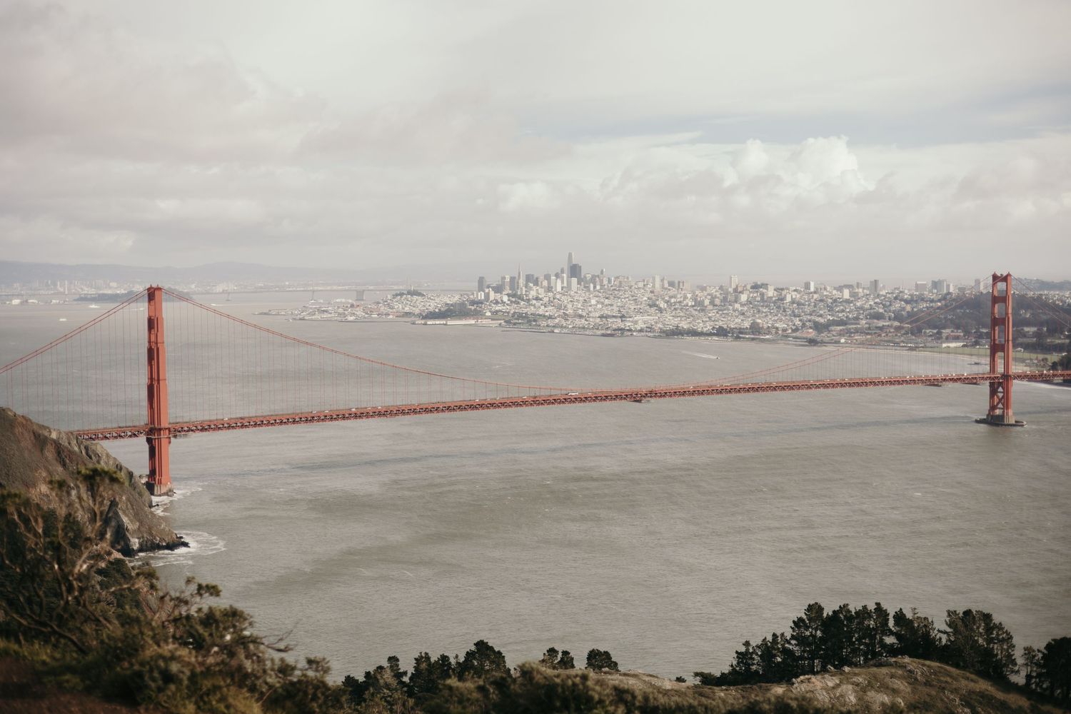 View of the Golden Gate Bridge spanning San Francisco Bay with city skyline visible in foggy background.