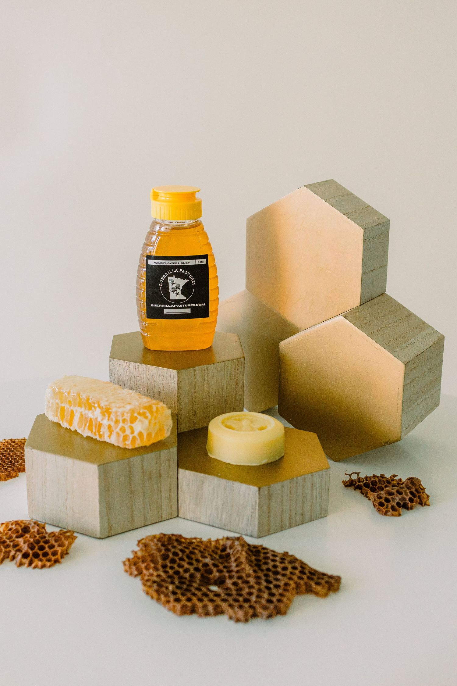 Honey bottle, honeycomb, and geometric wooden blocks arranged with scattered coffee beans in a minimalist display setup.