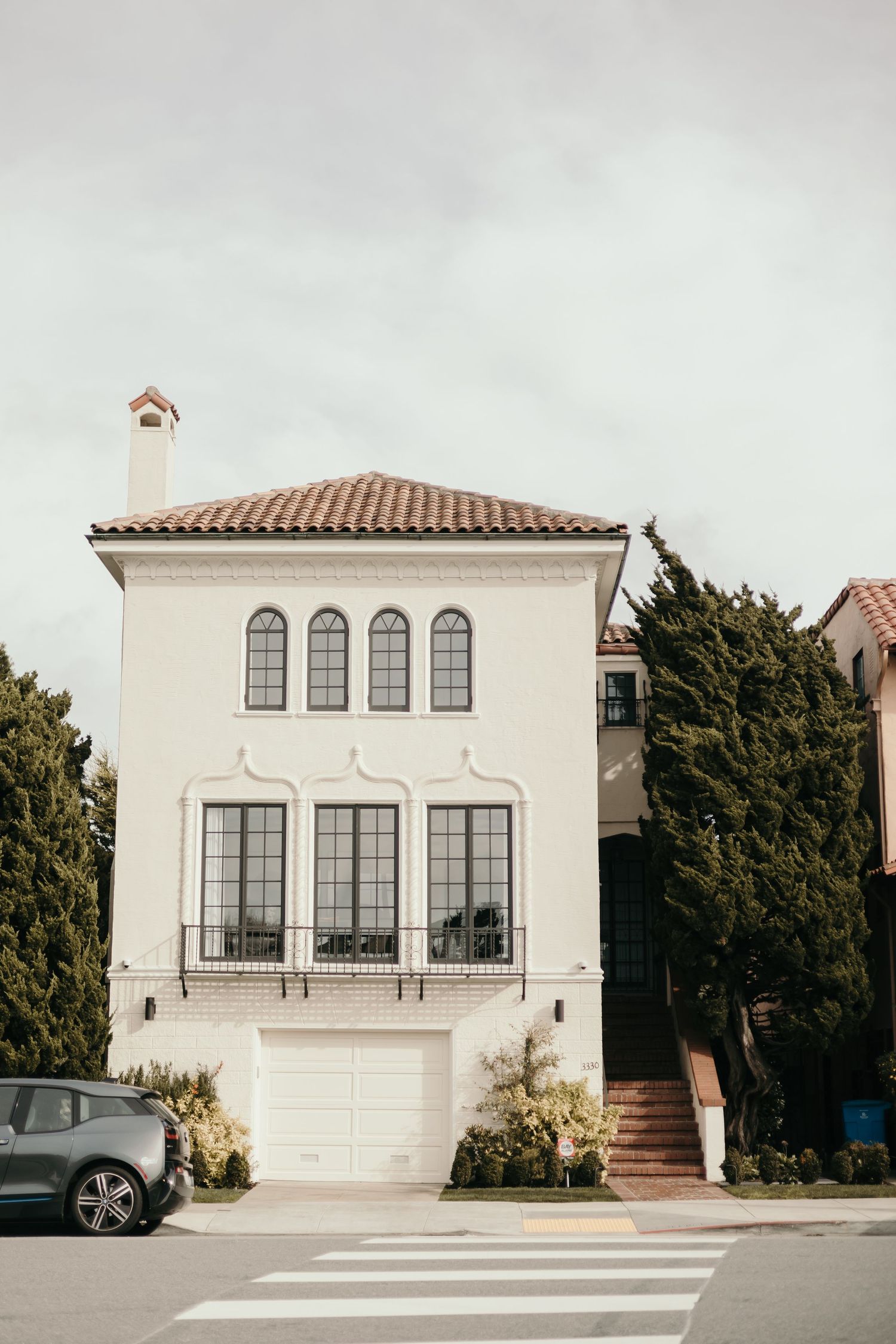 A white Mediterranean style house with arched windows and a terracotta roof in an urban setting.