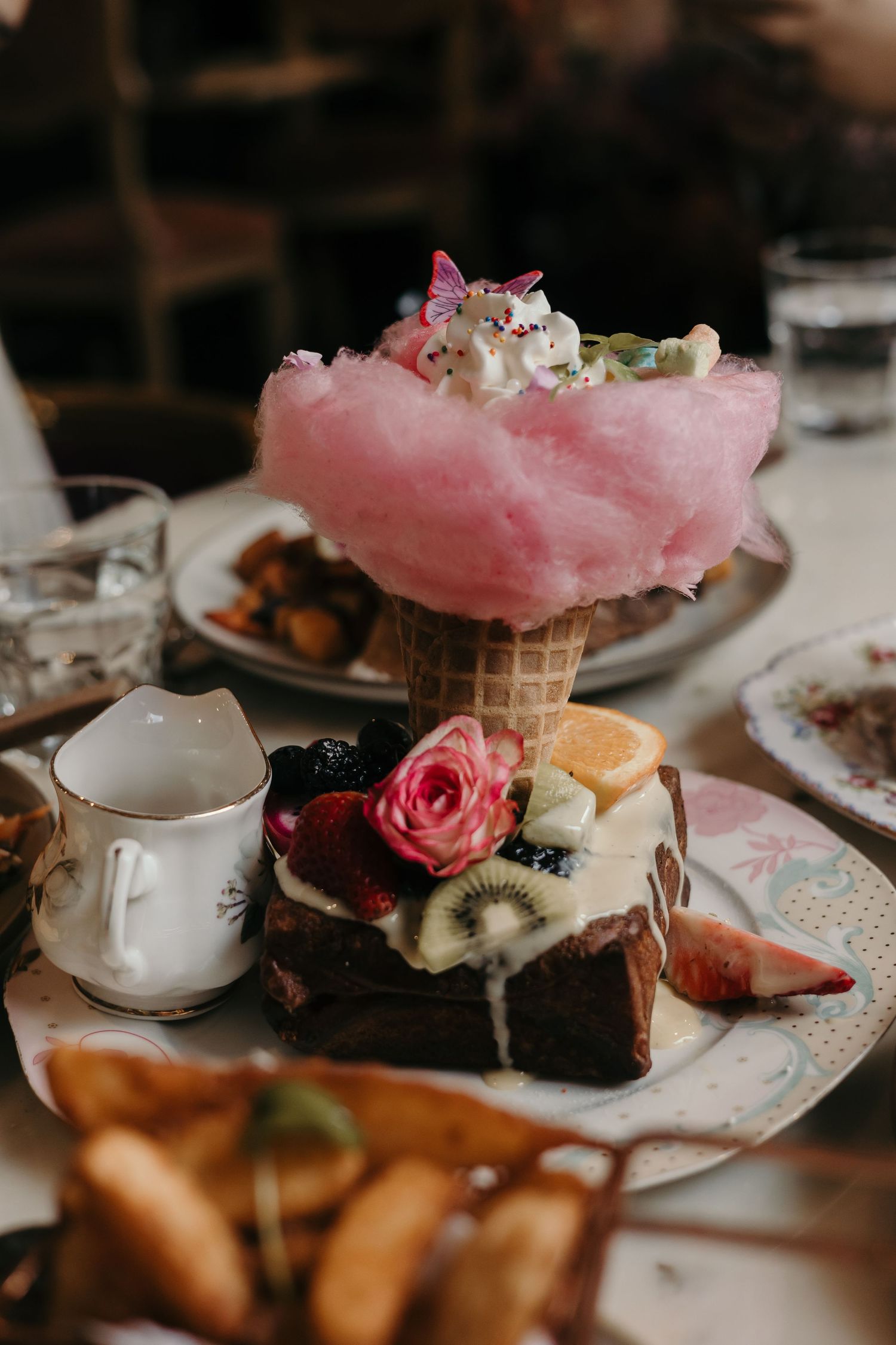 Pink cotton candy dessert served in a cone with rose garnish and chocolate cake slices.