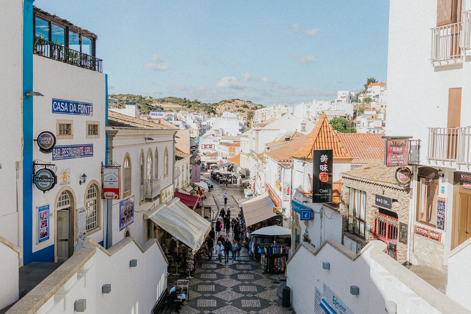 Charming cobblestone street lined with white buildings and shops in a Mediterranean coastal town.