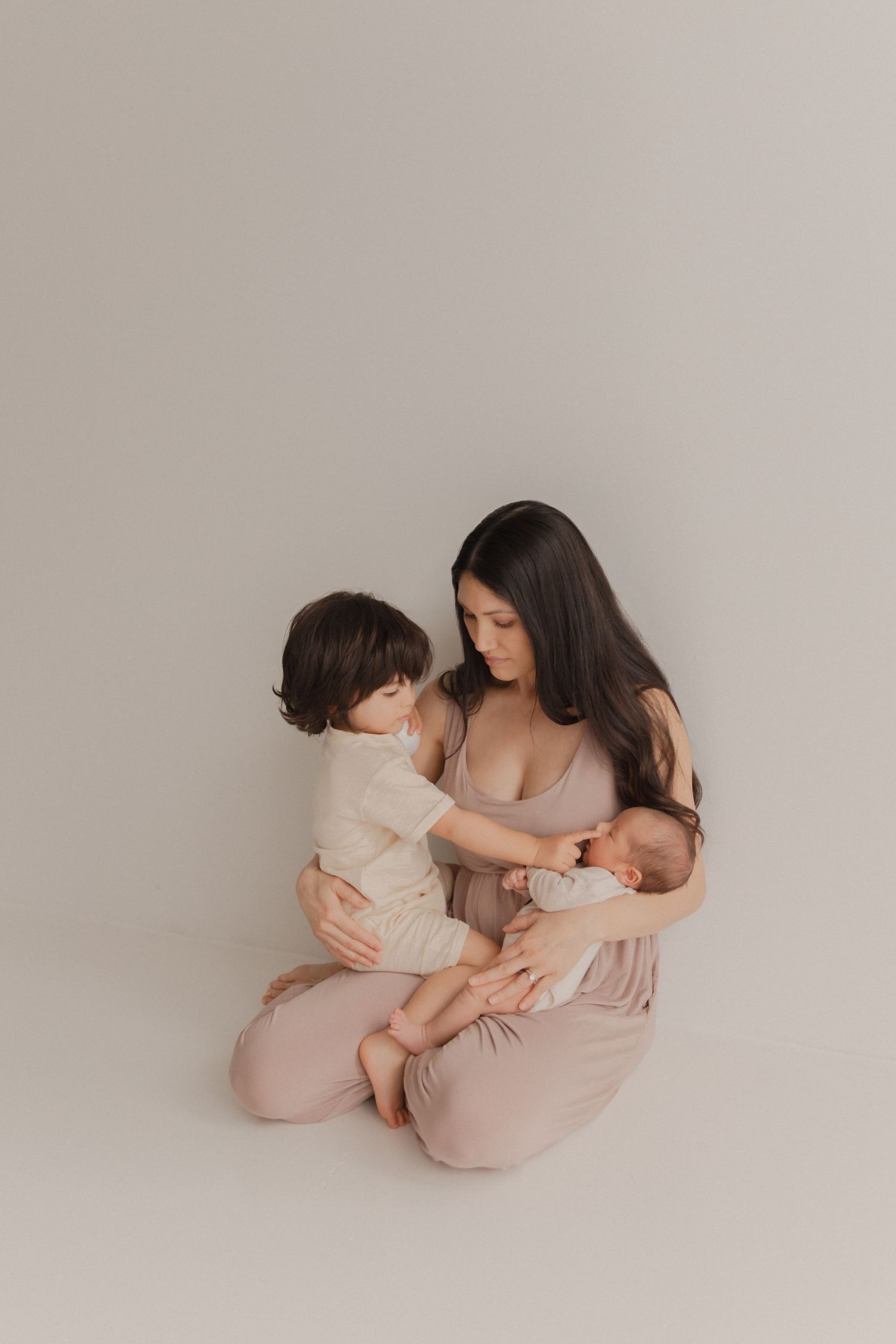 A tender family moment captured in soft pink tones as a mother bonds with her children against a neutral background.