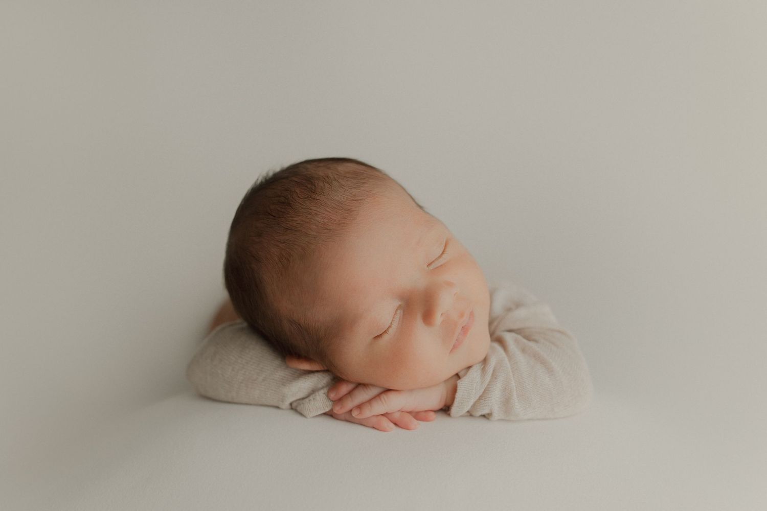 Newborn baby sleeping peacefully on white pillow in minimalist portrait setting.