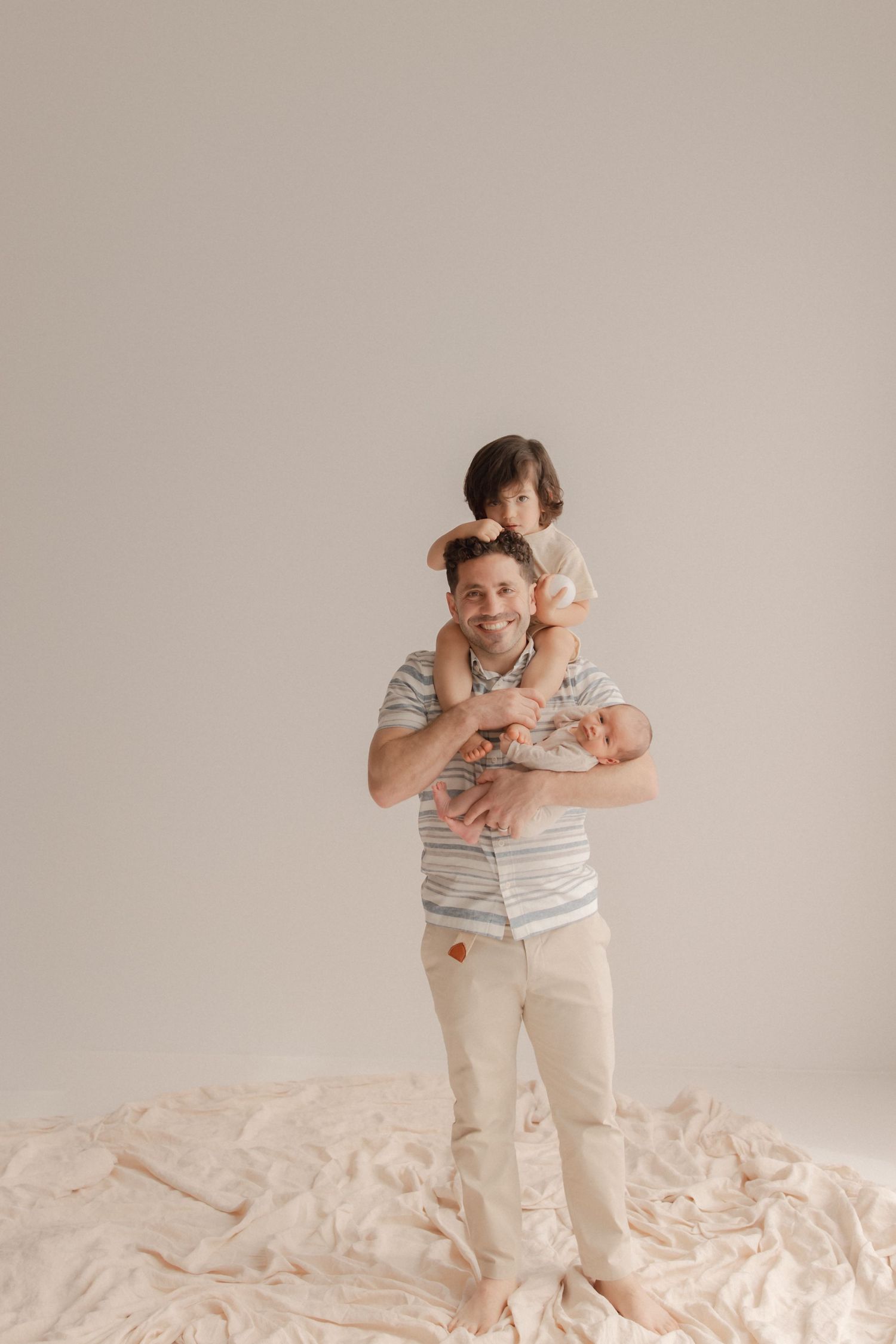 A gentle family portrait shows an adult holding a child on the shoulders against a neutral backdrop.