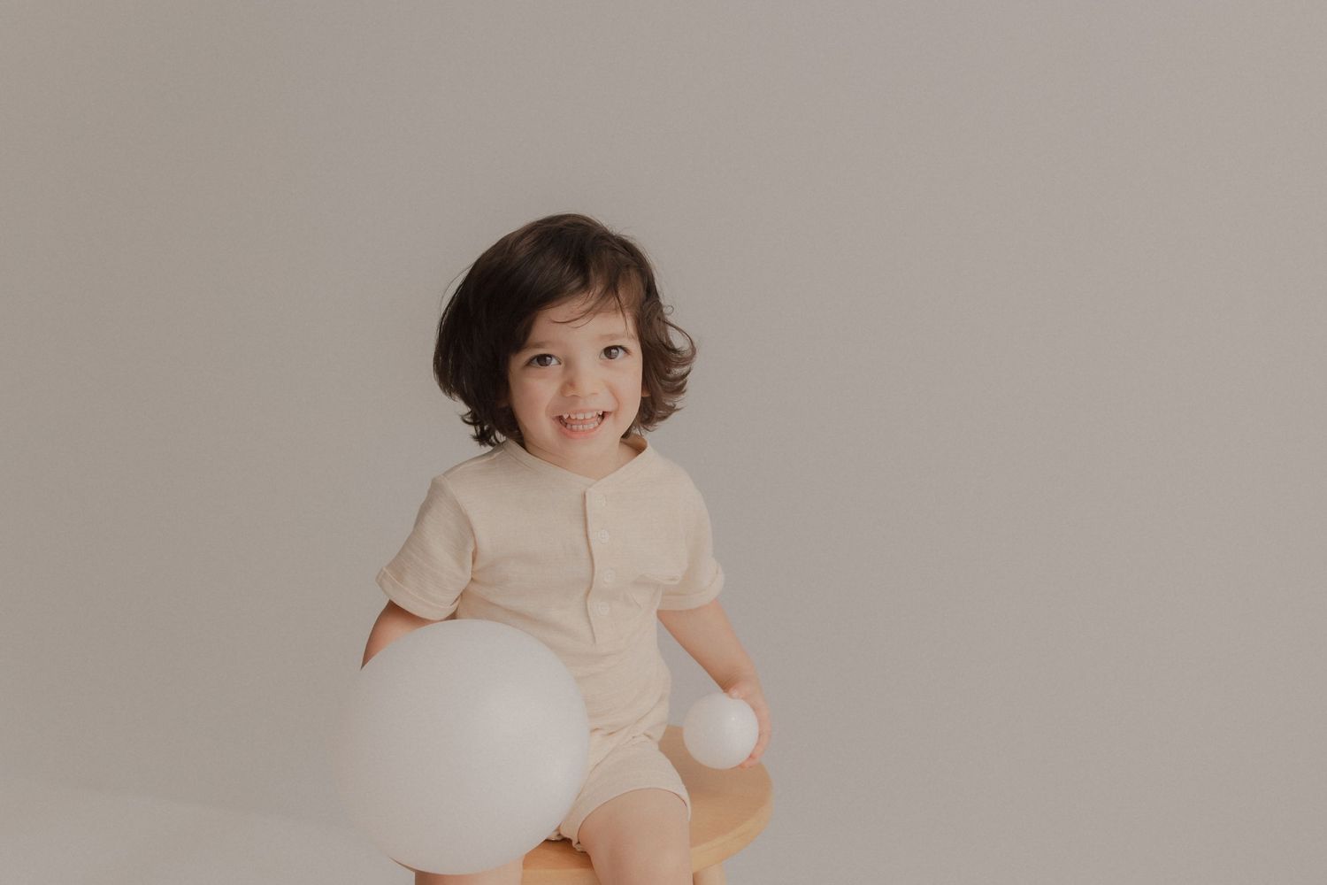 A child in a light-colored outfit sits on a plain background with a large white balloon.