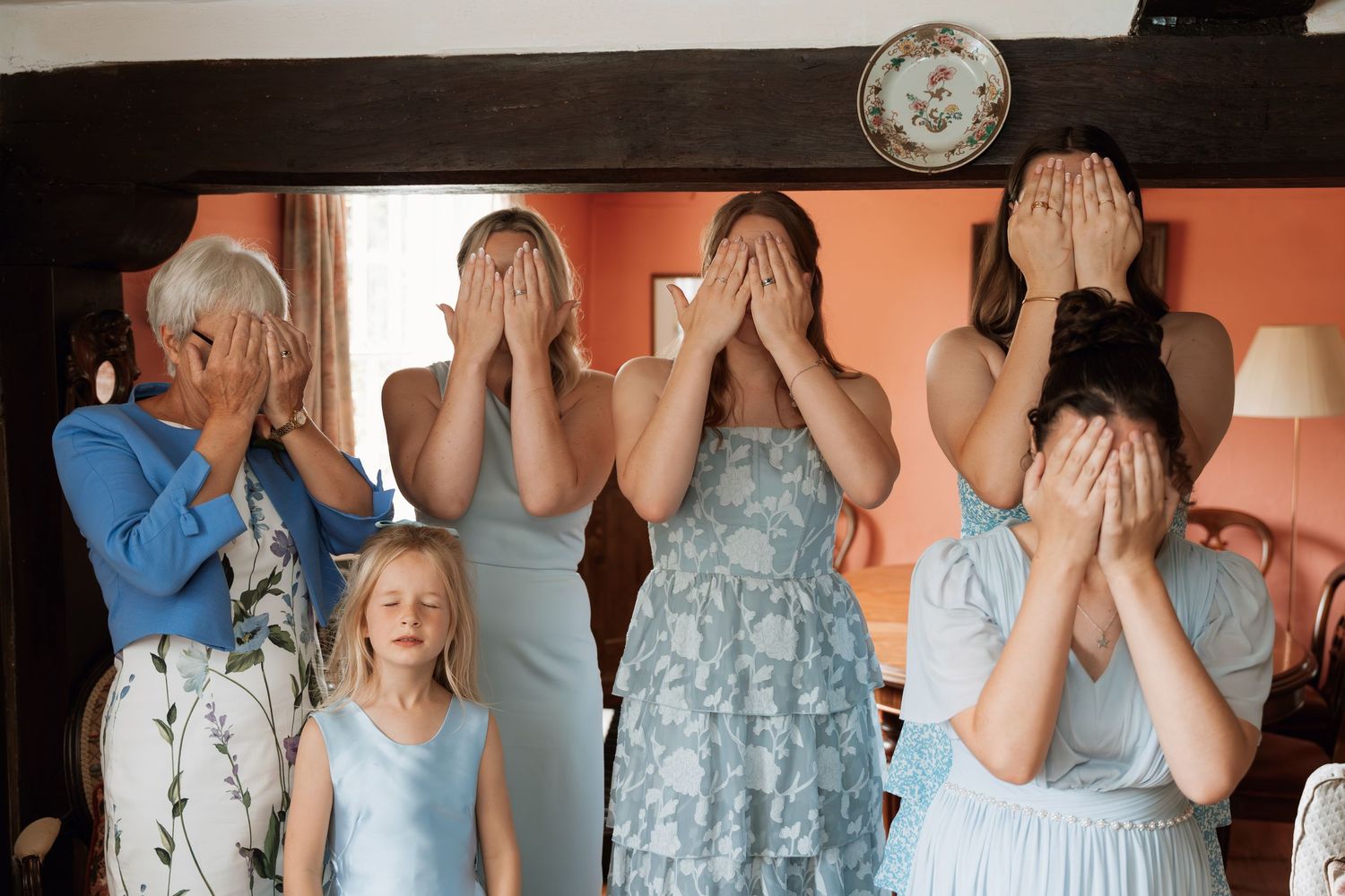 A group of people in formal attire stand in a row covering their faces with their hands.