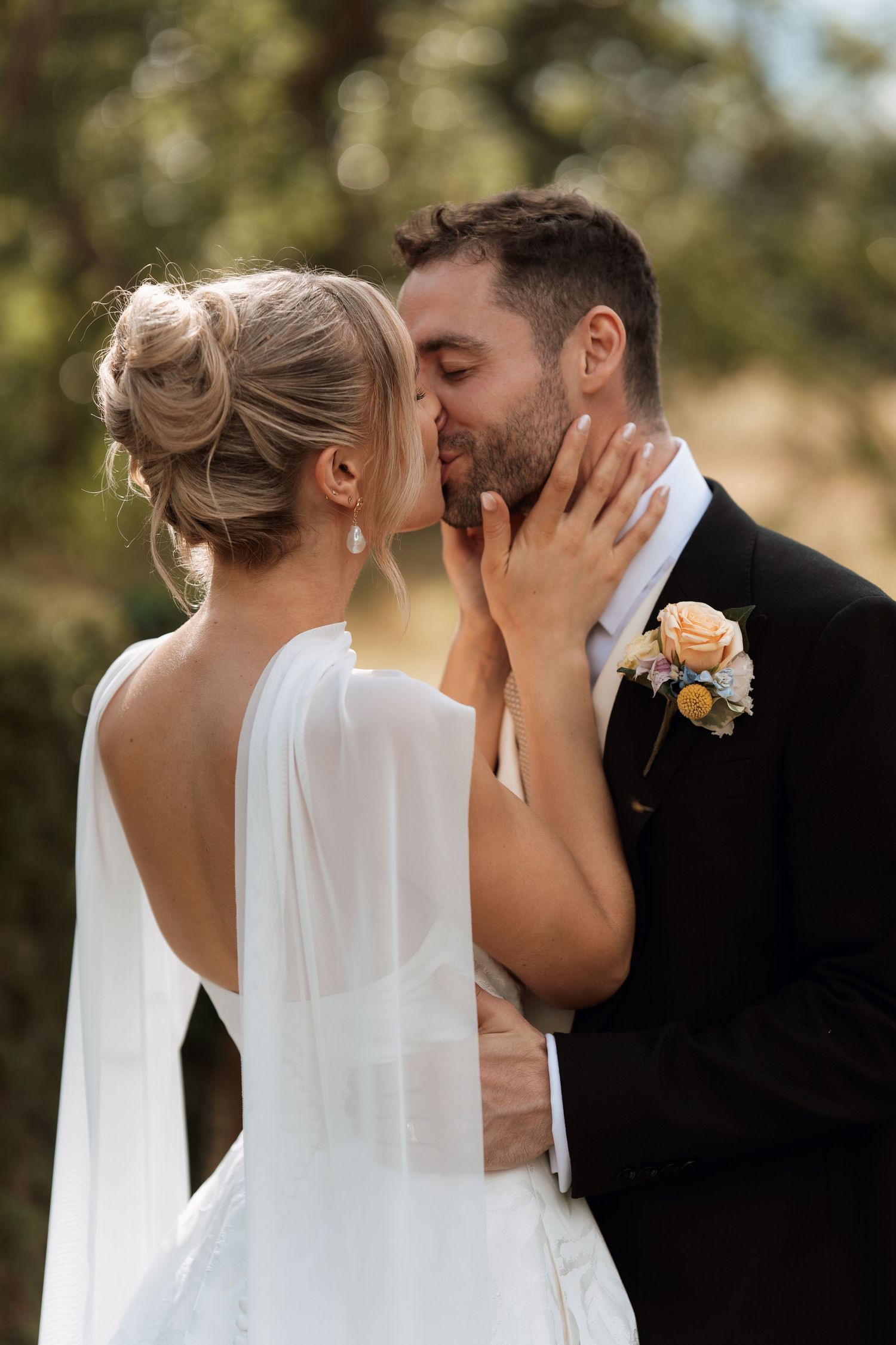 A romantic wedding moment captured in soft natural light with the couple sharing an intimate kiss.