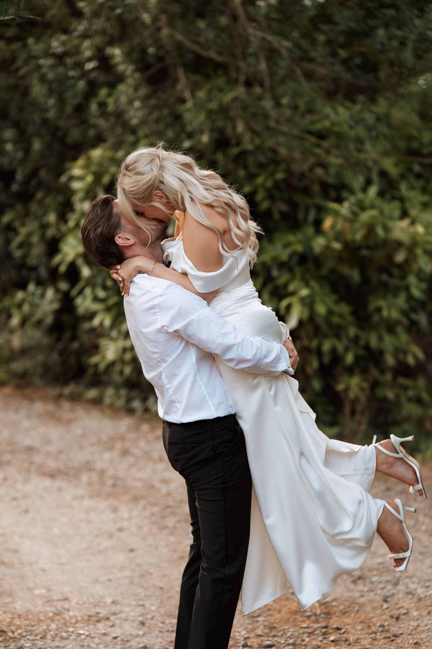 A couple shares an intimate embrace on a natural path surrounded by greenery.