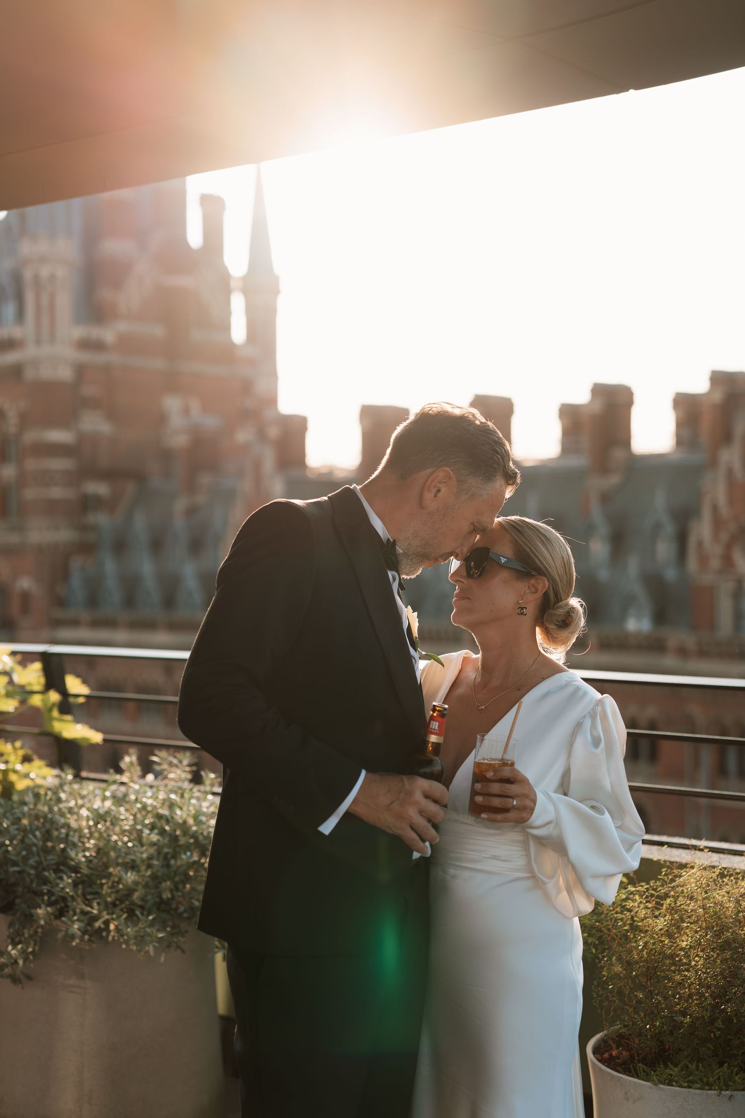 Newlyweds share a tender sunset moment on a rooftop with urban architecture in the background.