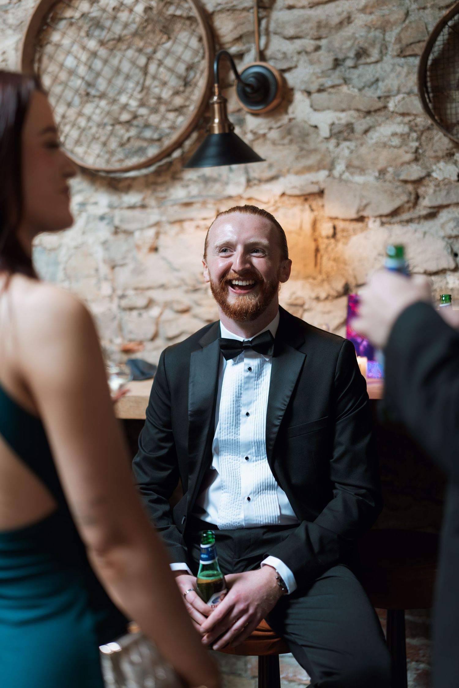 Guest in formal attire sitting against a rustic stone wall at a wedding reception.