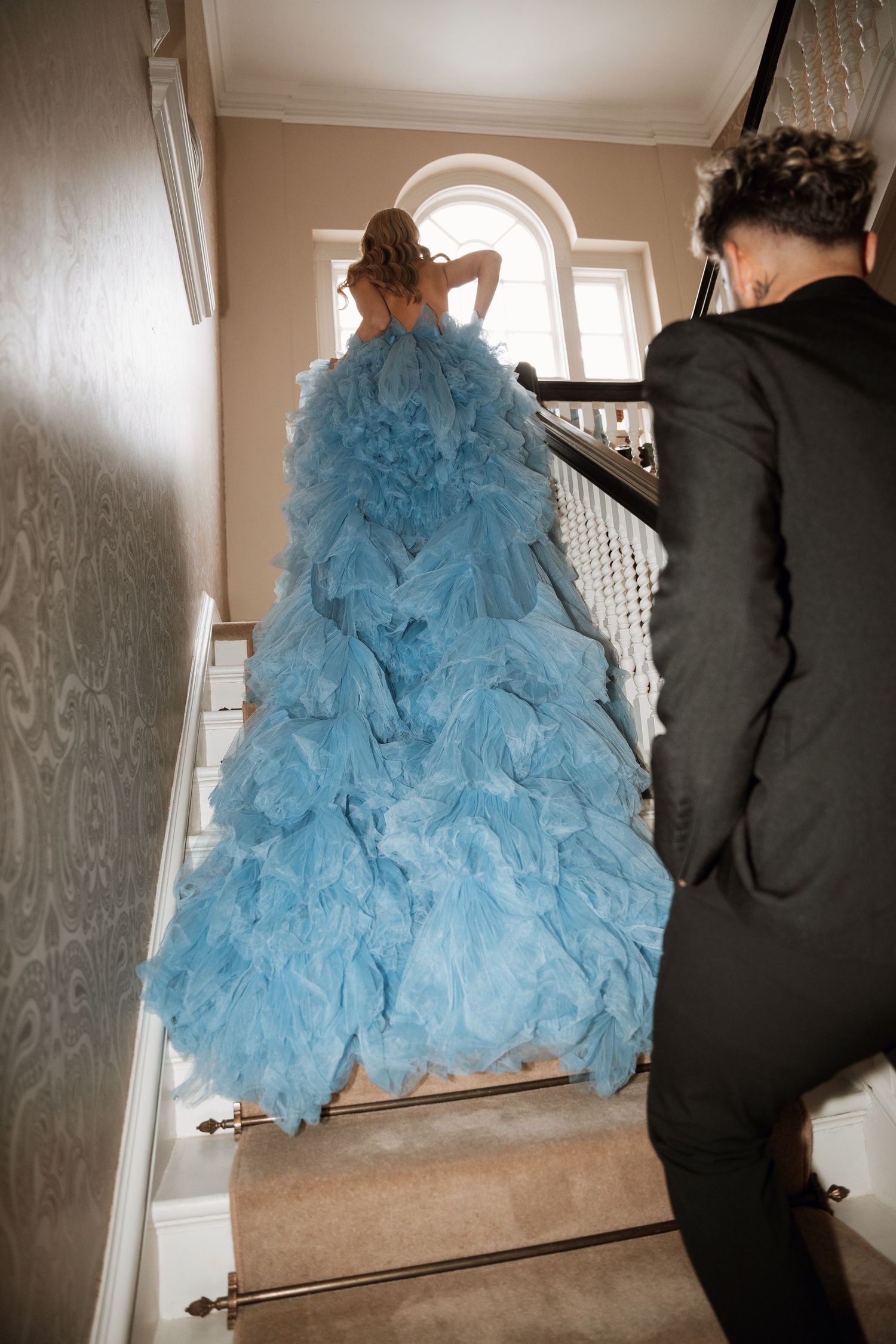 A flowing light blue tulle gown cascades down a staircase during a formal event.