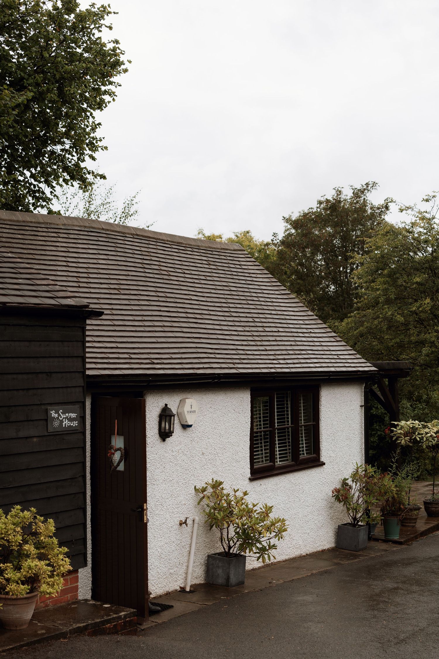 White bungalow with black trim and sloped roof surrounded by trees and landscaping.