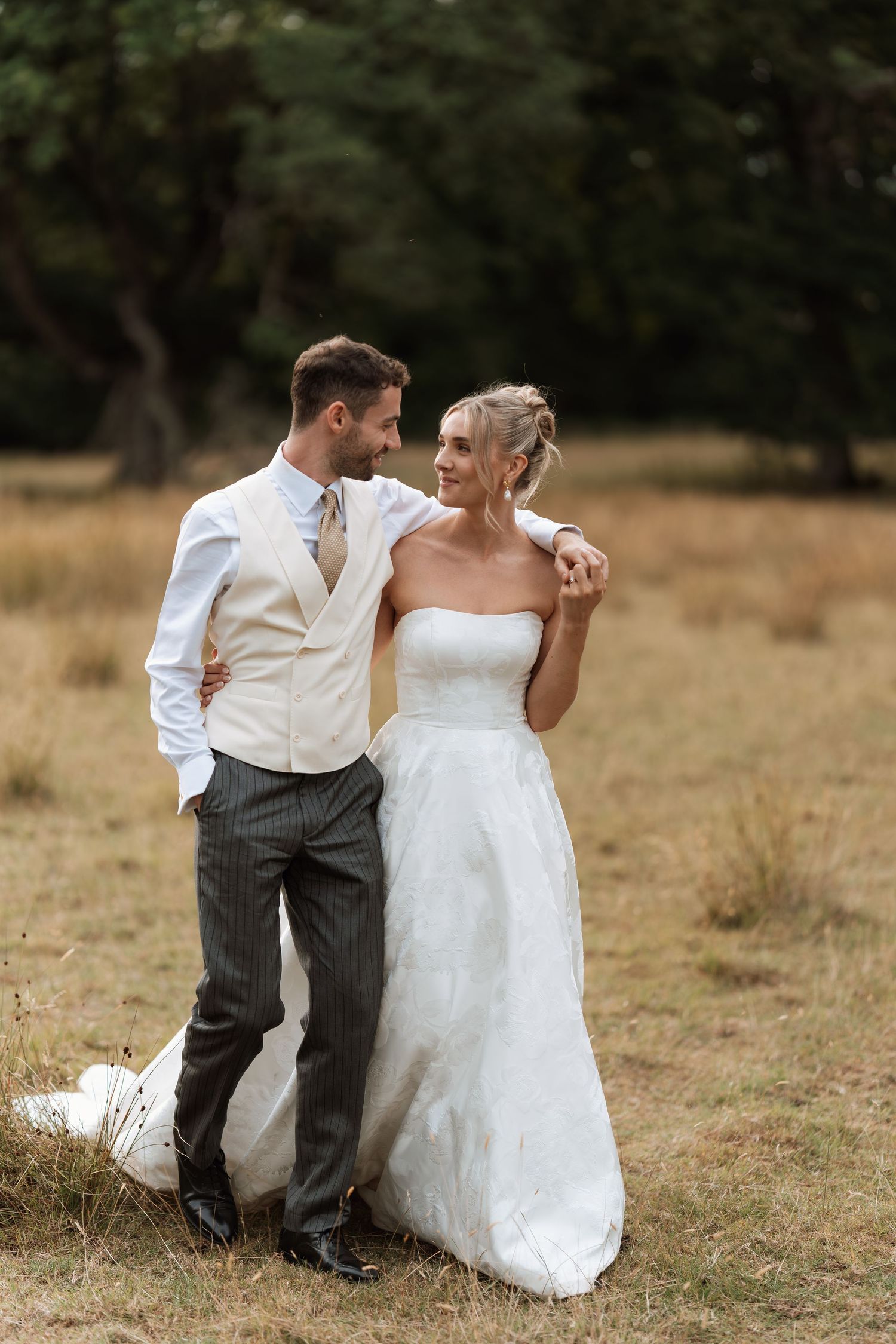 A romantic wedding portrait of a couple standing in a rustic field with trees in the background.