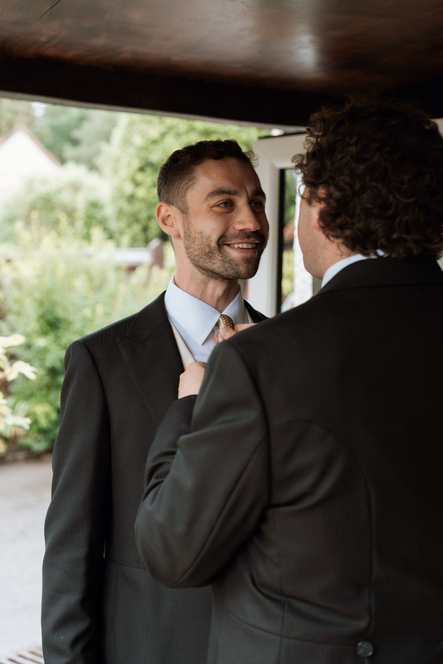 Two people in formal suits share an intimate moment before their wedding ceremony.